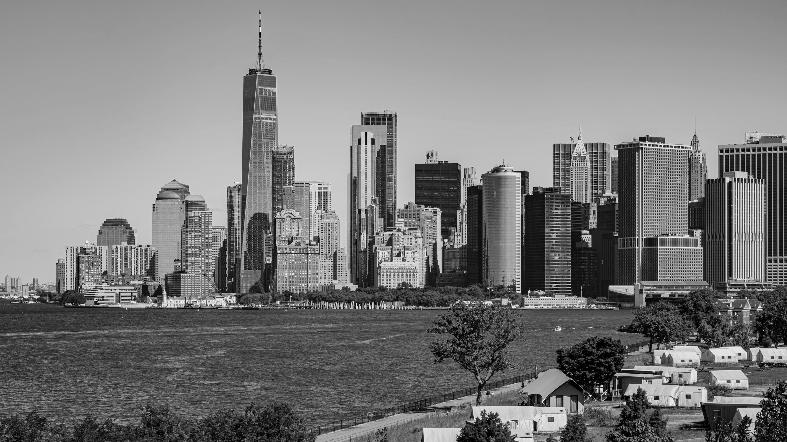 Black and white photograph of the New York City skyline across the river, with tall skyscrapers and buildings. Manhattan, New York, USA.