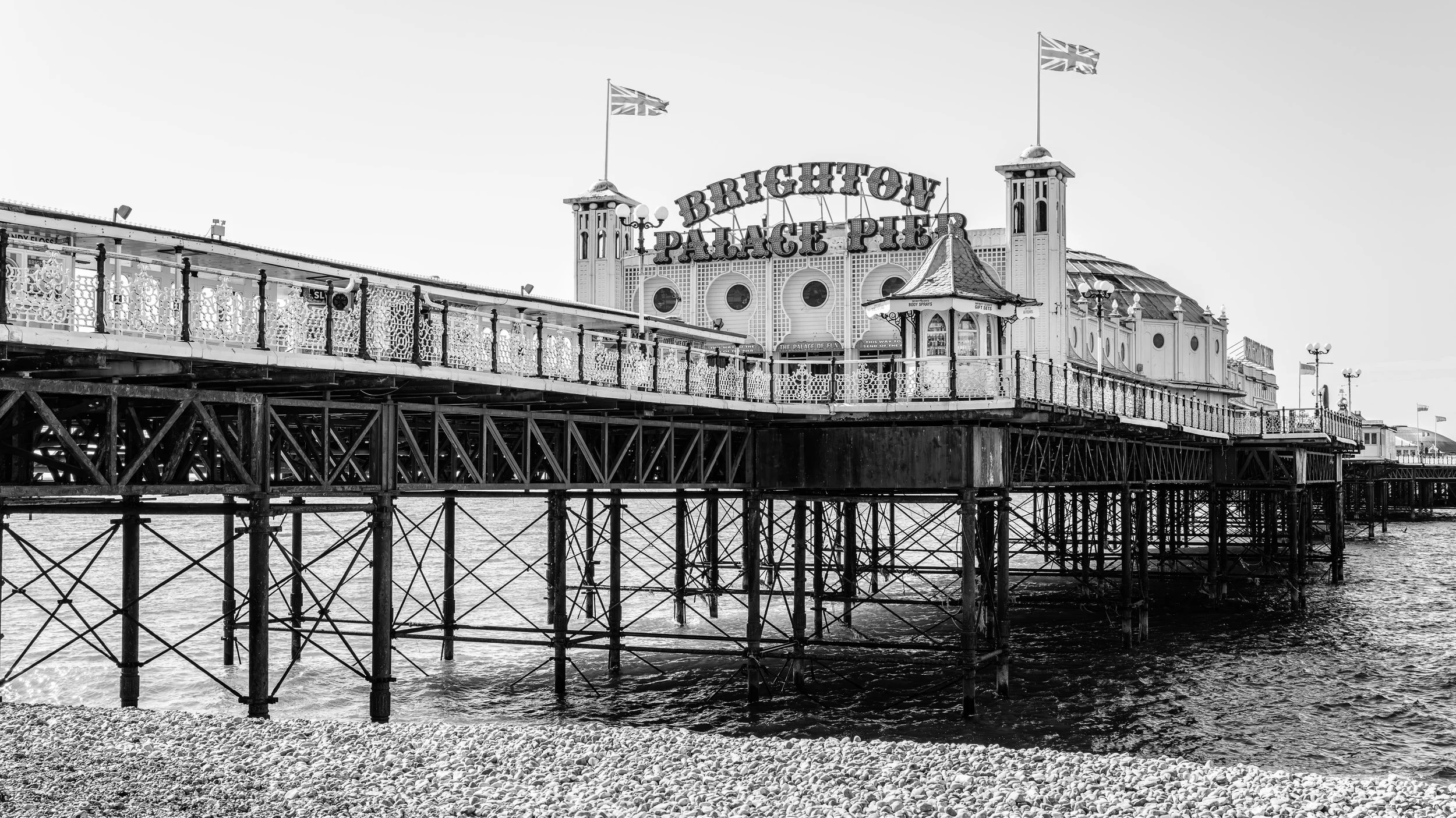Black and white photo of Brighton Palace Pier showing the pier structure, flags, and sign.