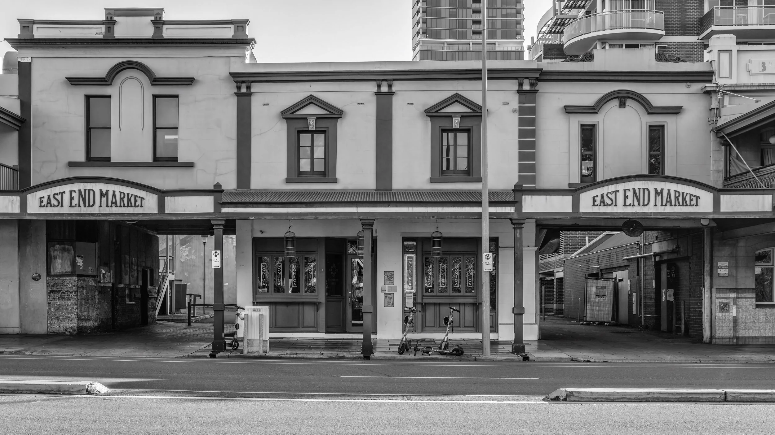 Front of a building with a sign that reads 'East End Market,' with two electric scooters parked outside, in black and white. Adelaide, Australia.