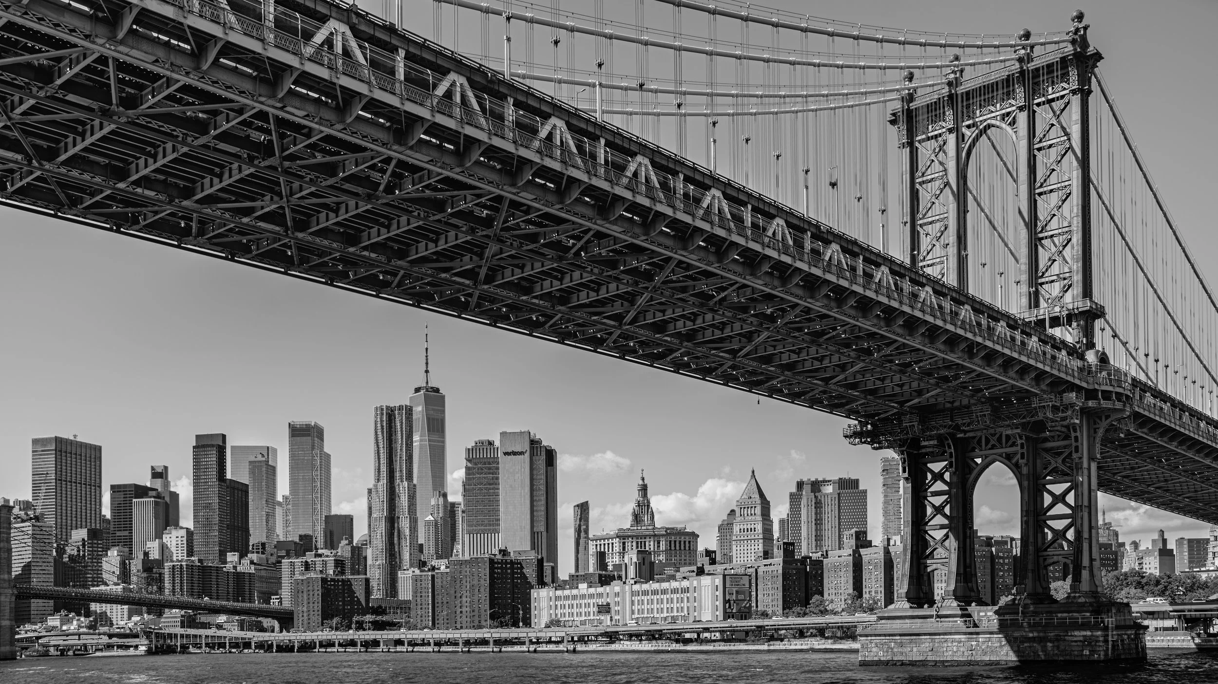 Black and white photo of a city skyline with tall buildings and a large suspension bridge in the foreground. Manhattan Bridge, Manhattan, New York, USA.