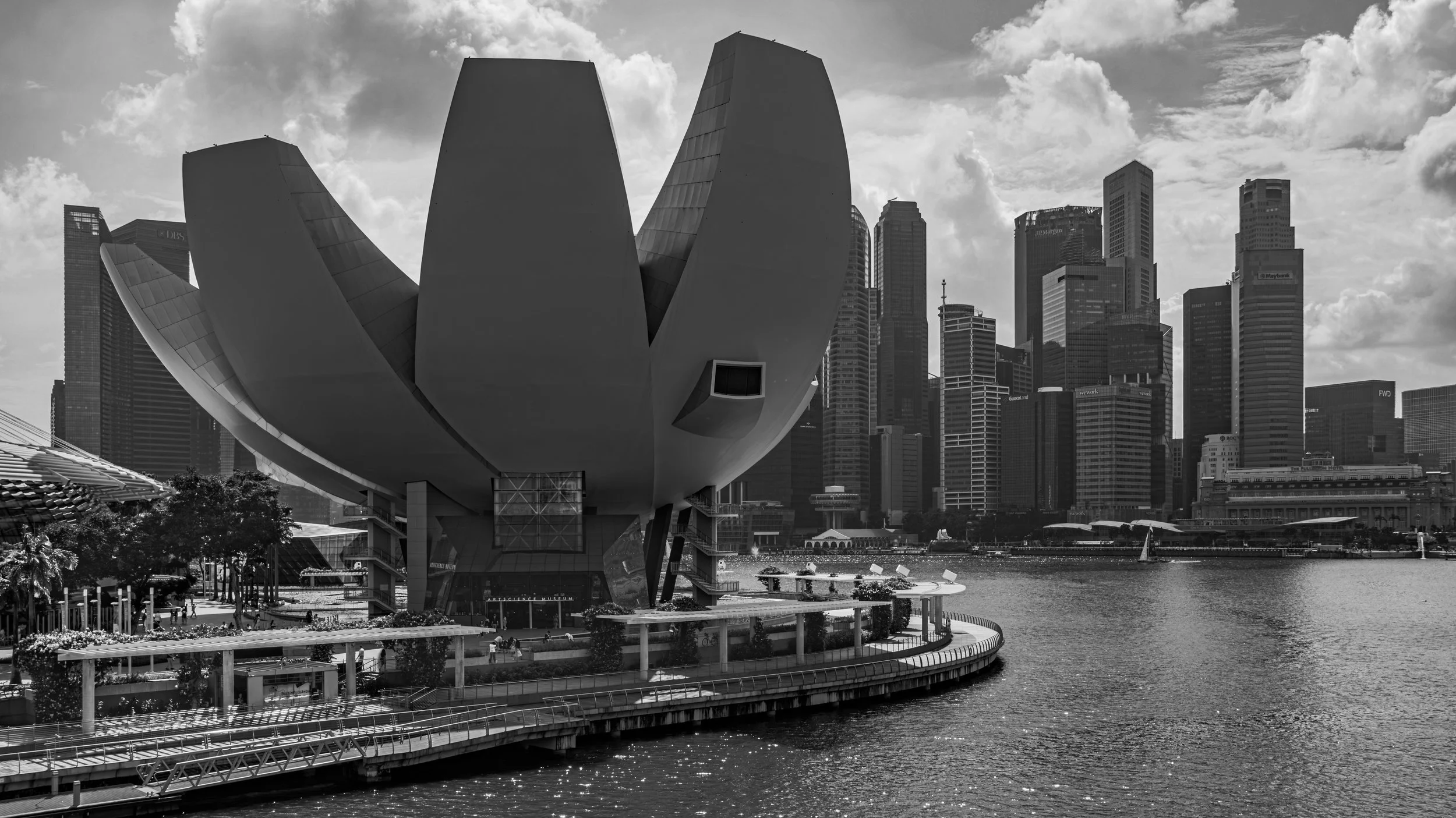 Black and white photo of Singapore ArtScience Museum with futuristic design, surrounded by city skyscrapers and a river in the foreground.