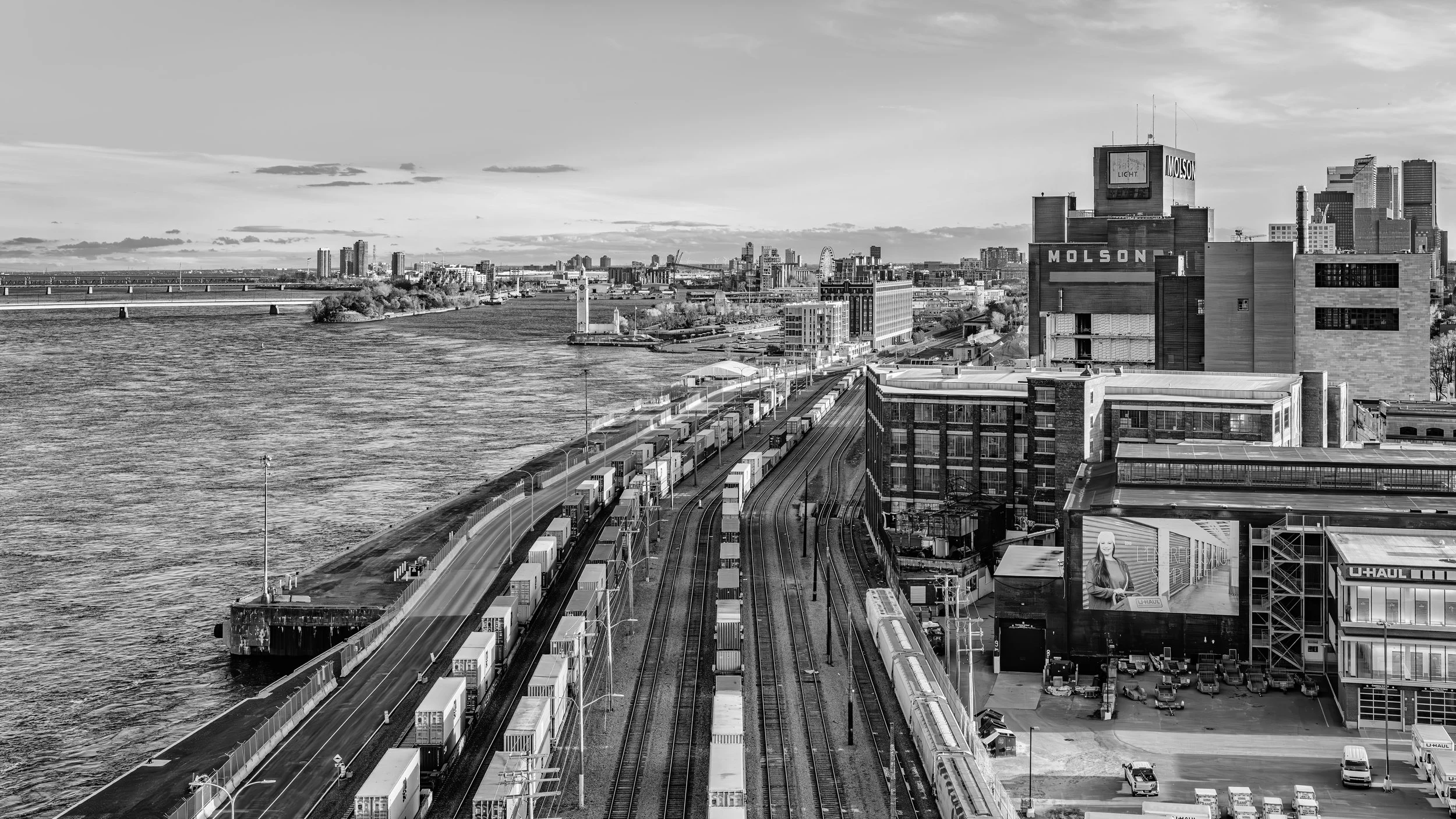 Black and white cityscape skyline featuring a river, train tracks with containers, and high-rise buildings including a Molson building
