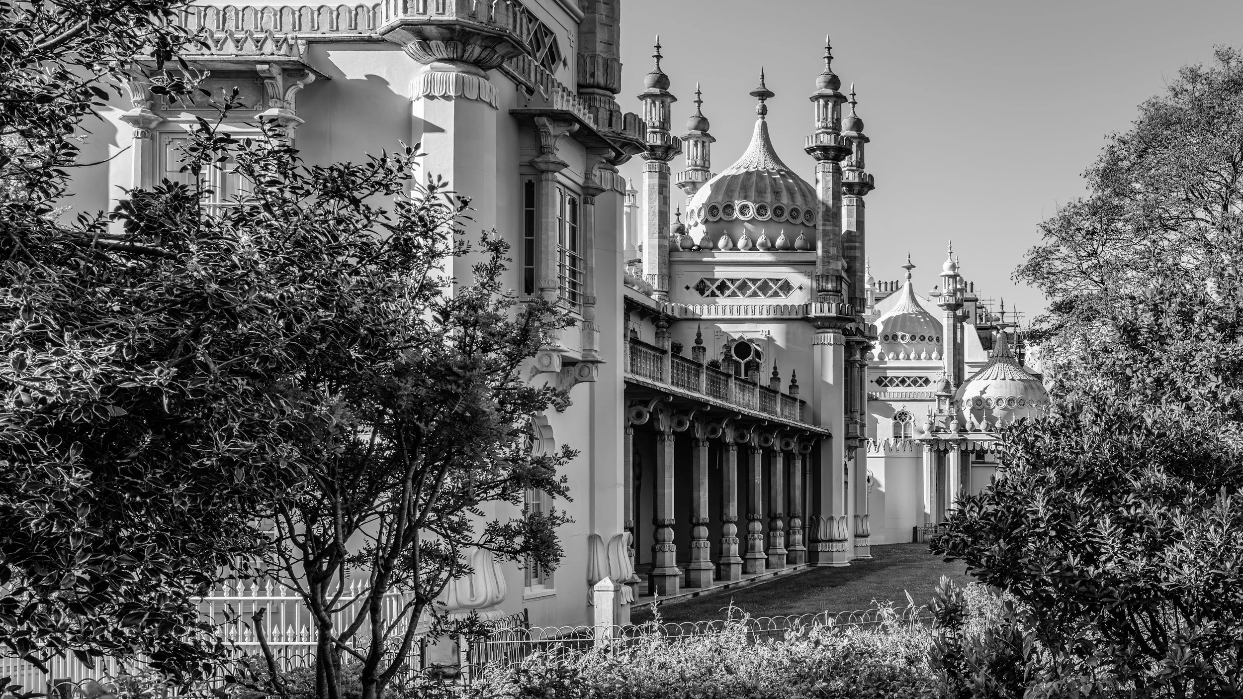 Black and white photo of an ornate castle or palace with domes and towers, partly obscured by trees and foliage.