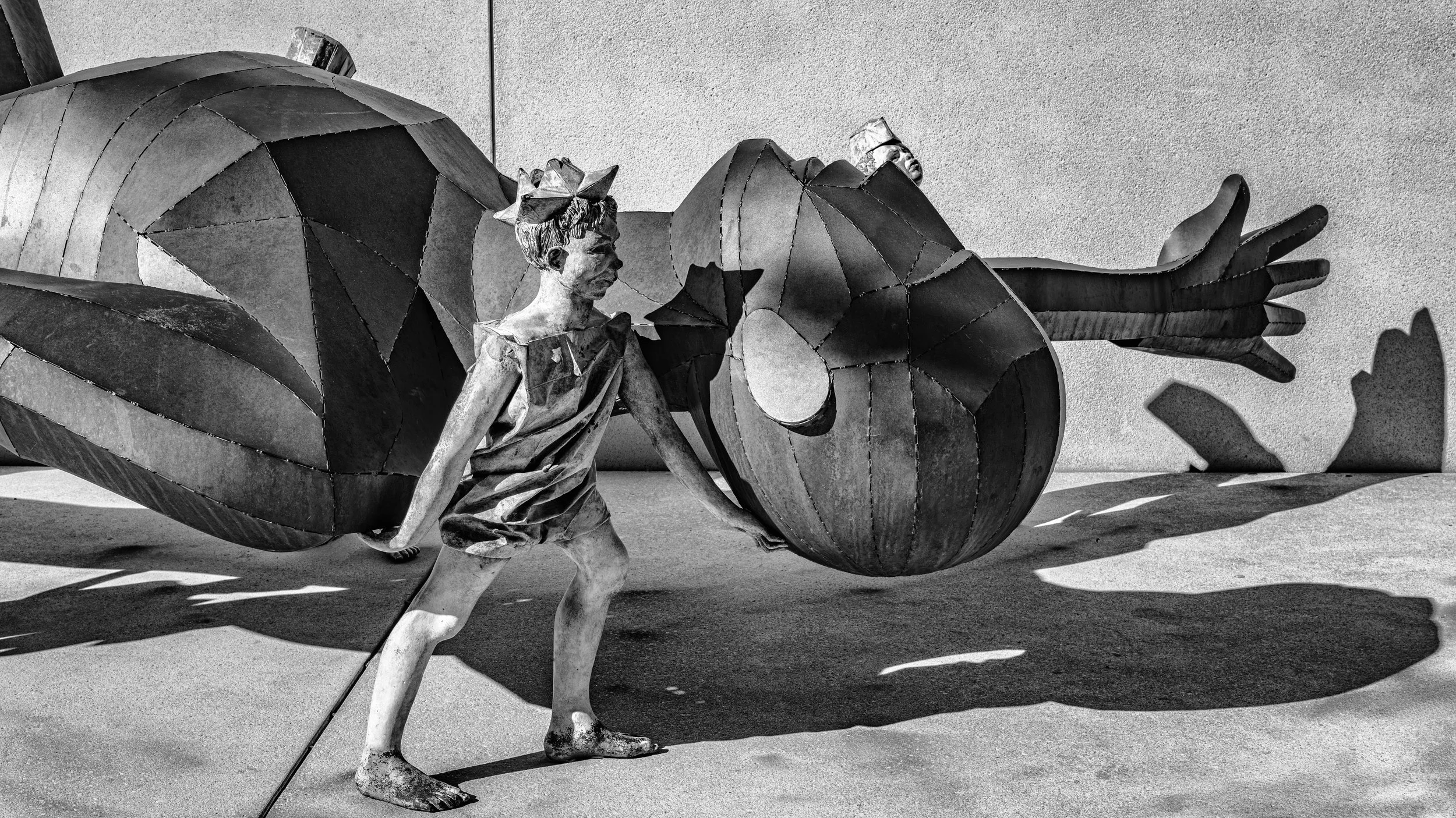 Black and white sculpture featuring a woman with a large insect with prominent wings, possibly a beetle or butterfly, and stylized hand shapes in the background.
