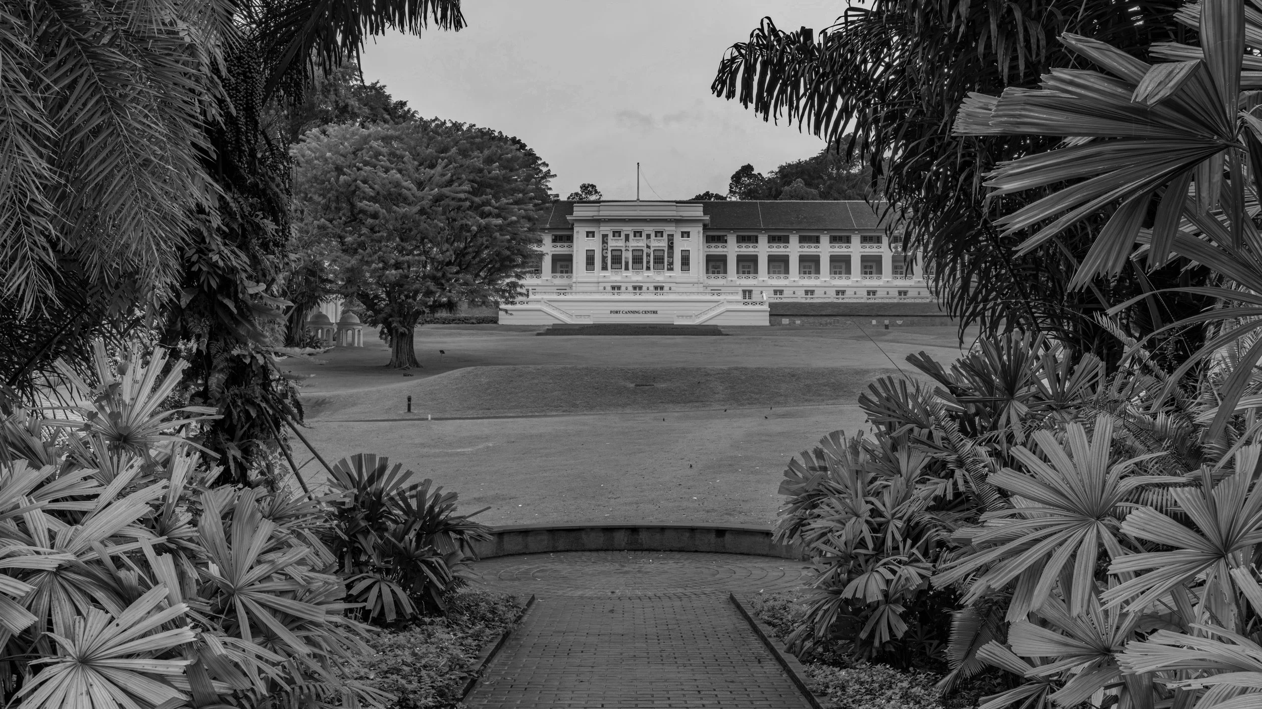 Black and white photo of Fort Canning Centre viewed through lush tropical plants and trees.