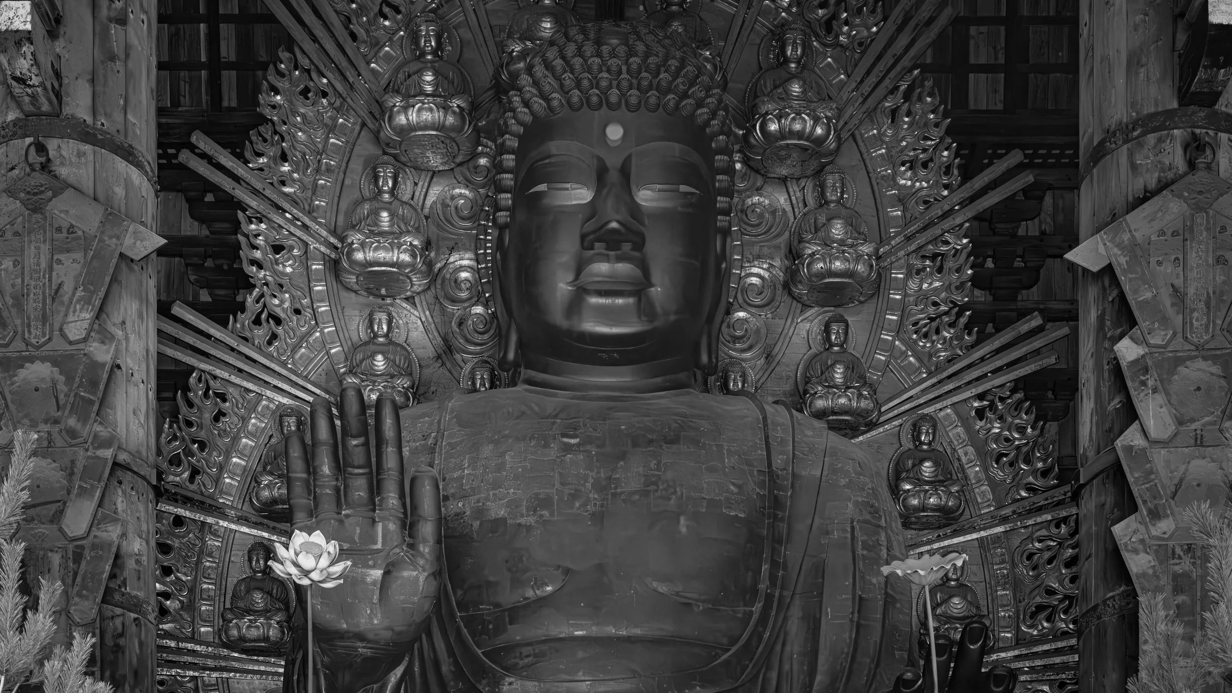 A large Buddha statue with a serene face, surrounded by smaller Buddha figures and intricate decorative elements, in an indoor setting.