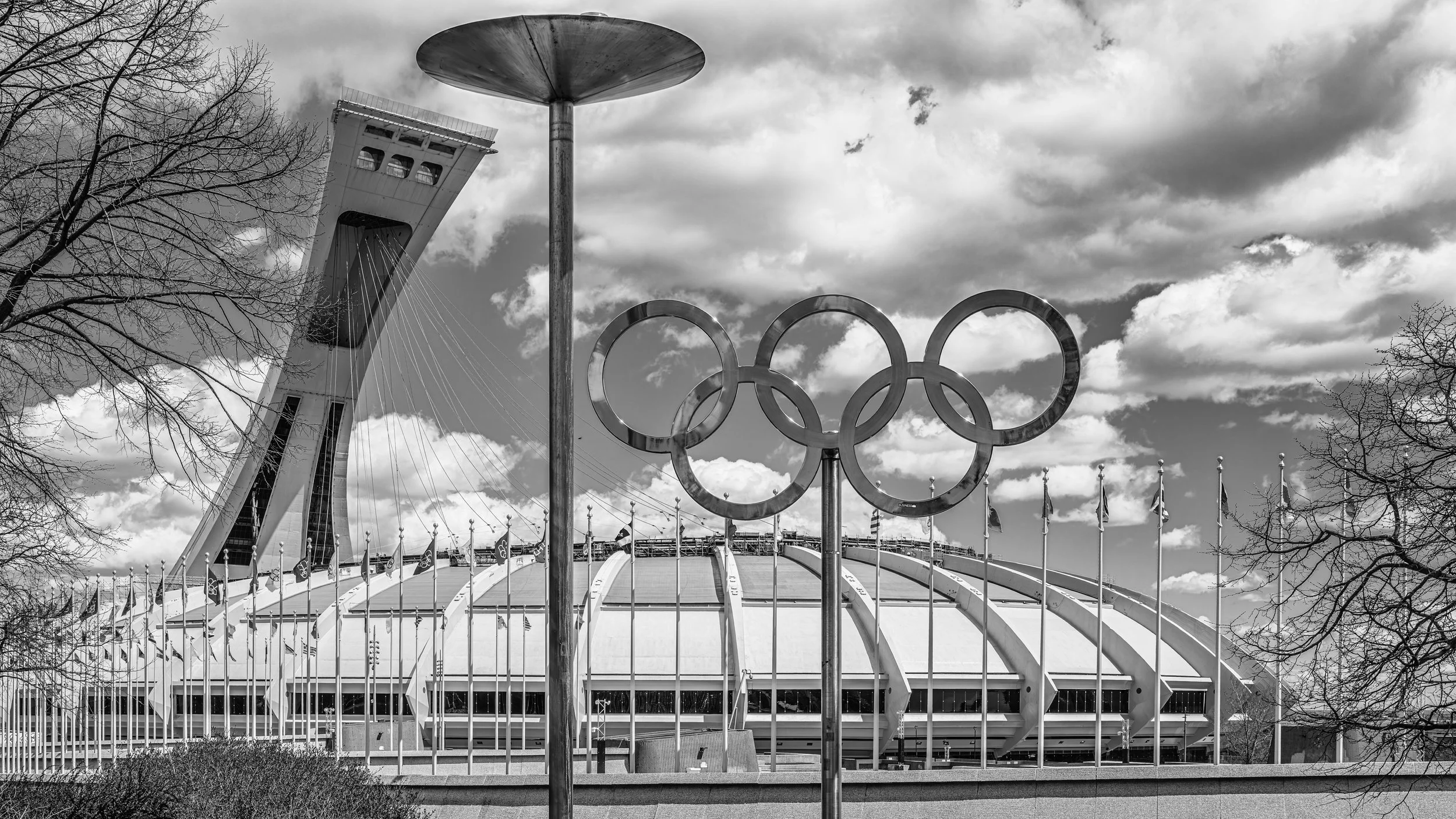 Black and white photo of the Millennium Tower and the Olympic rings in Seattle, Washington, with trees and clouds in the background.