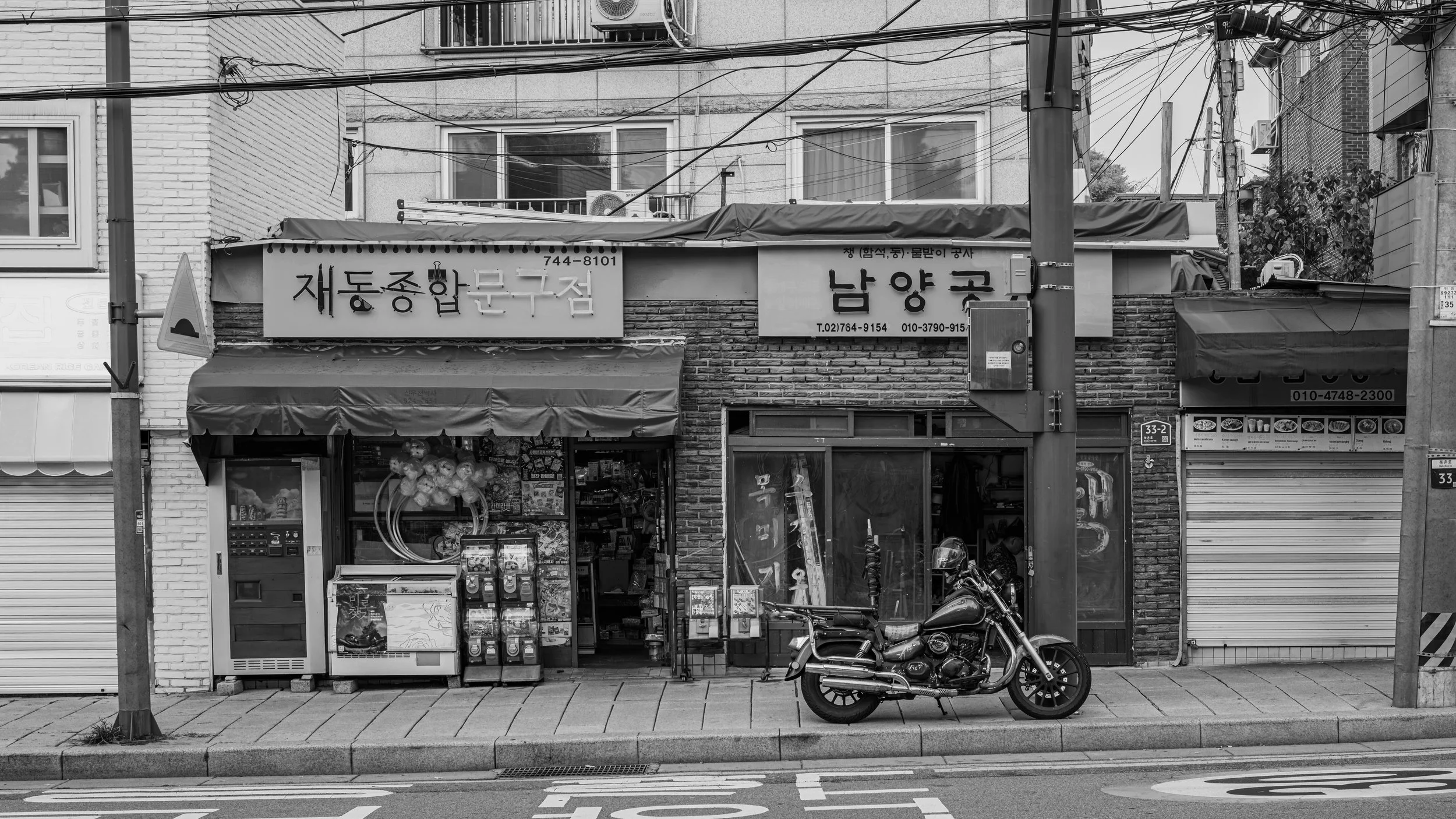 Street view of a storefront in an urban area with signs in Korean, a motorcycle parked in front, and overhead electrical wires.