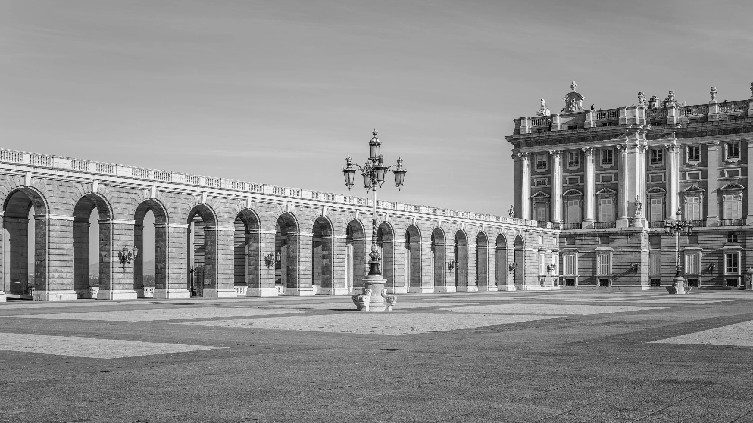 Black and white photo of a European-style palace with detailed architecture, including columns and statues, and an open courtyard with a decorative lamp post.