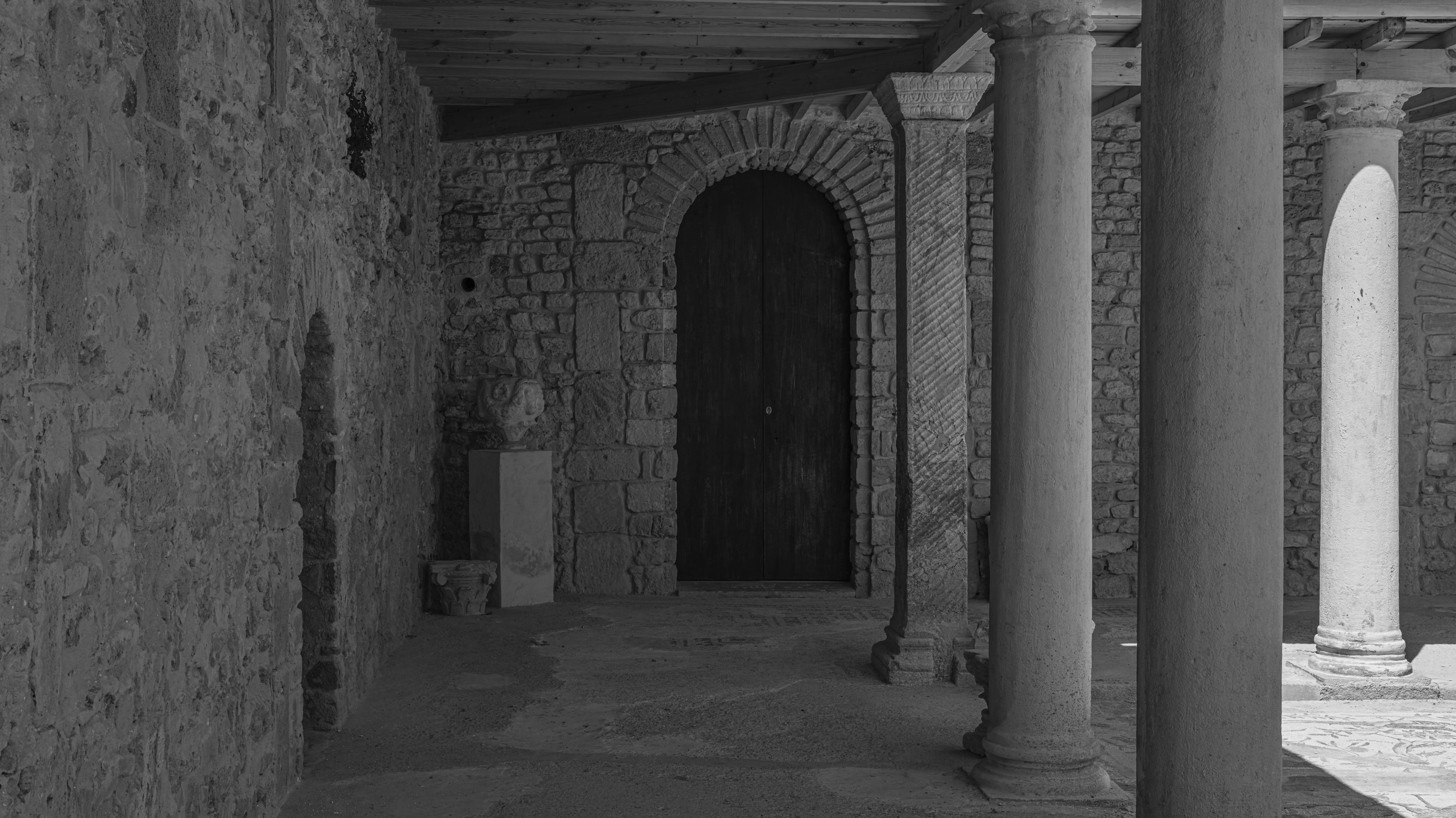 Black and white photo of ancient stone columns and an arched door inside a historical building.