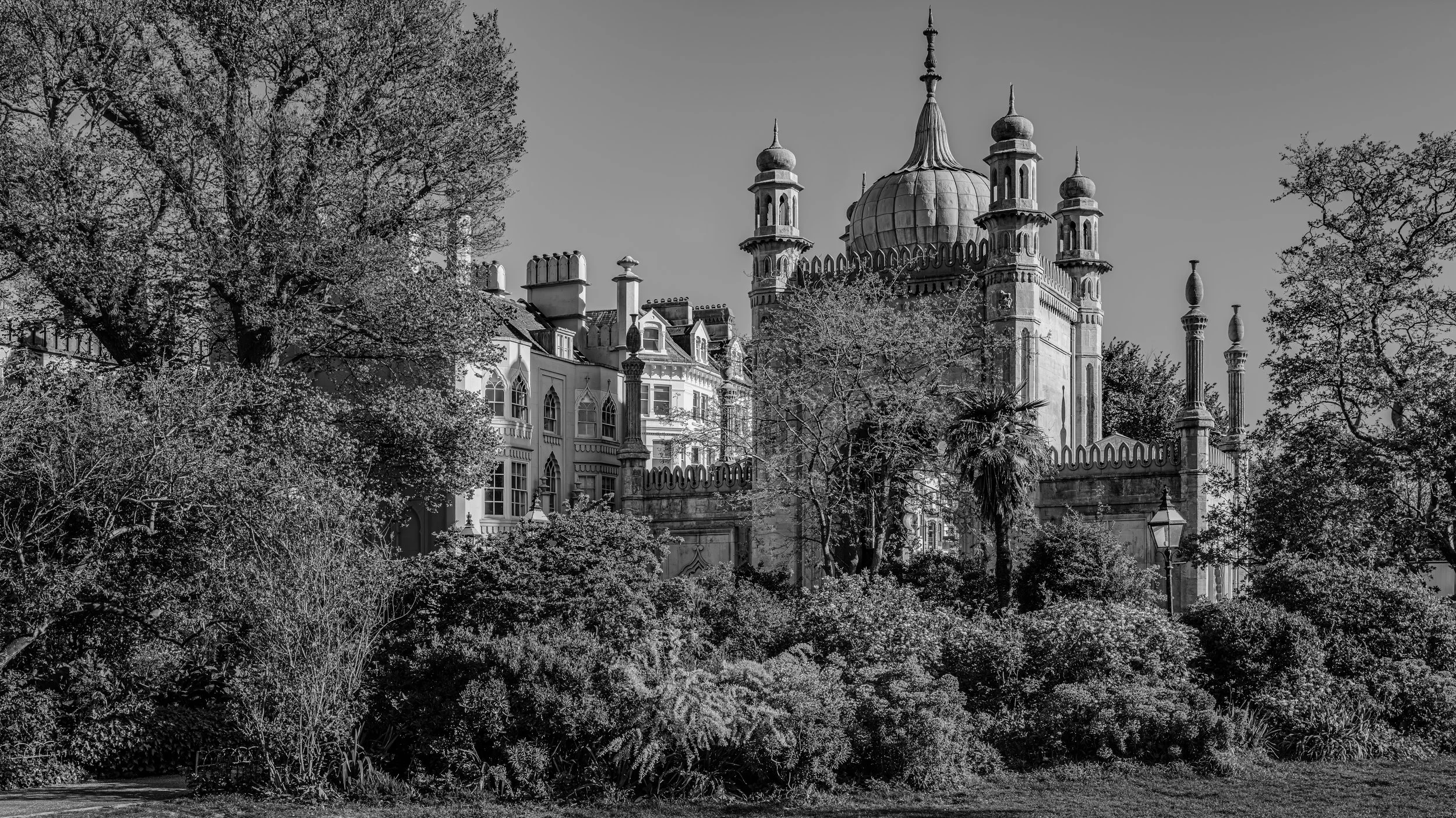 Black and white photo of a historic building with domes and minarets, surrounded by trees and a stone fence with decorative posts.