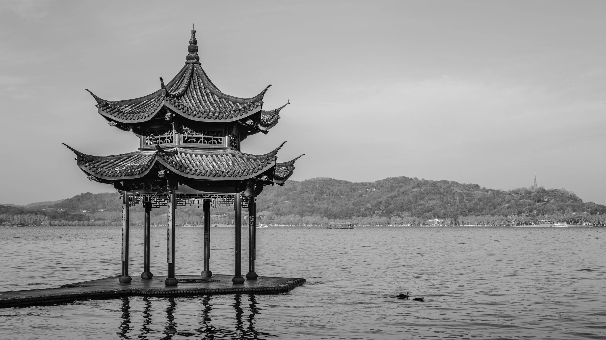 A traditional Chinese pagoda on a lake with hills in the background, black and white photo.