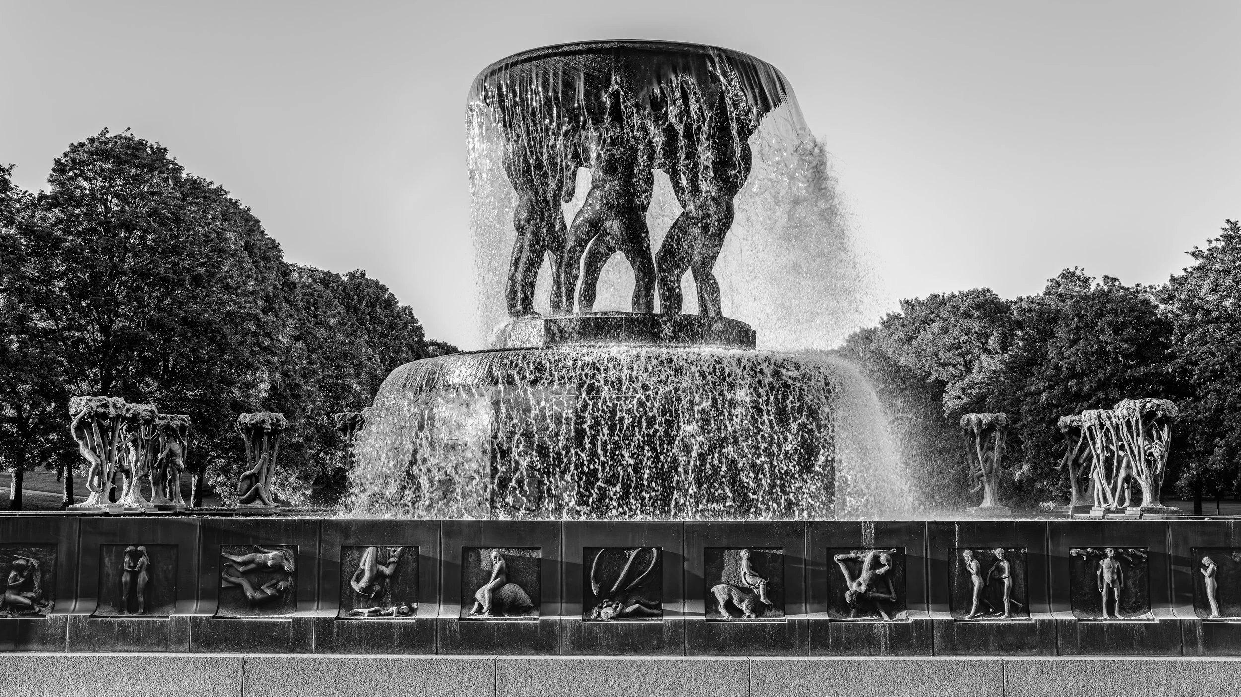 A large fountain featuring bronze sculptures of human figures surrounded by trees.
