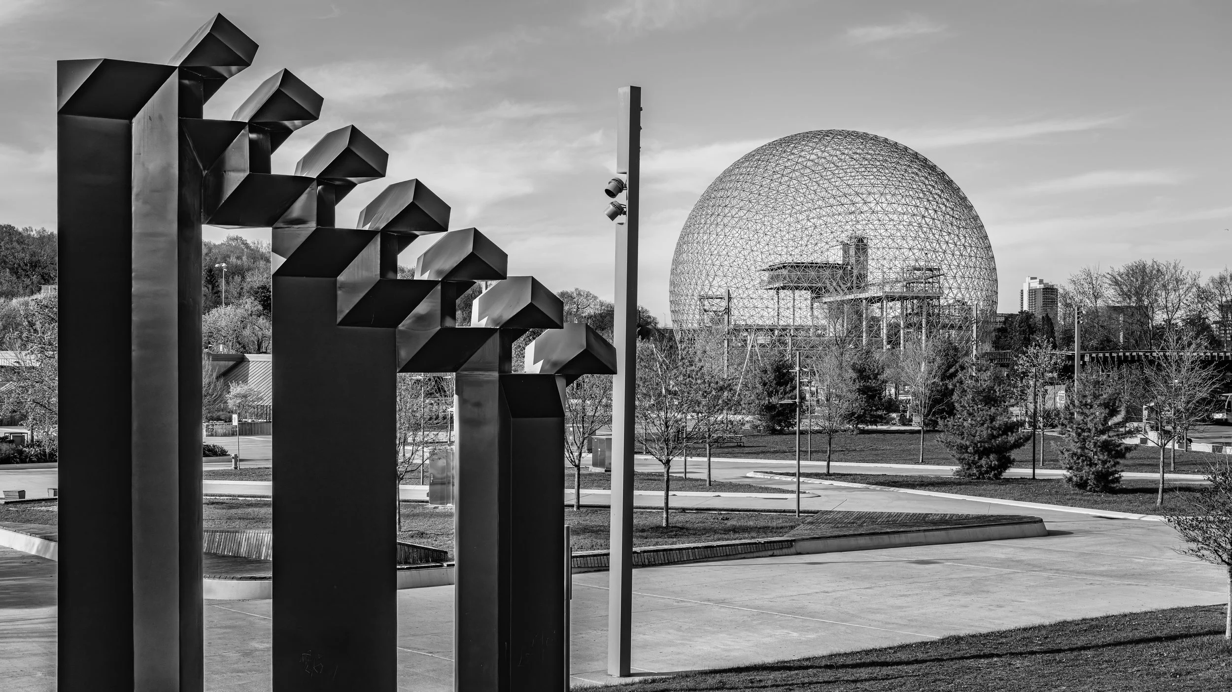 Black and white photo of modern sculptures in a park with a geodesic dome in the background