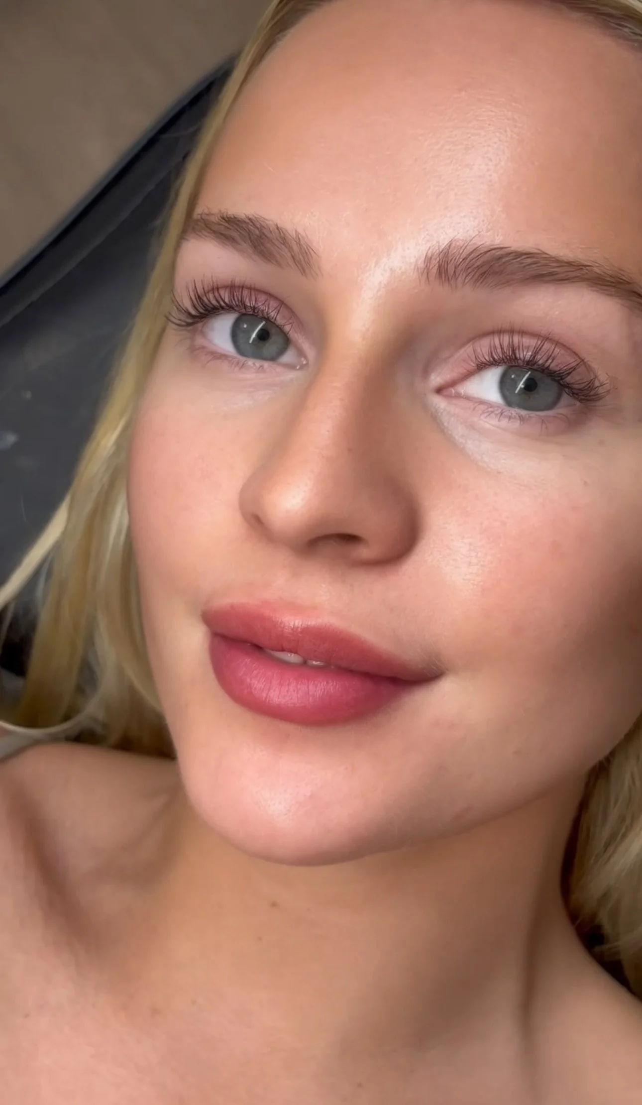 Close-up of a young woman with blue eyes, blonde hair, and light makeup, smiling softly.