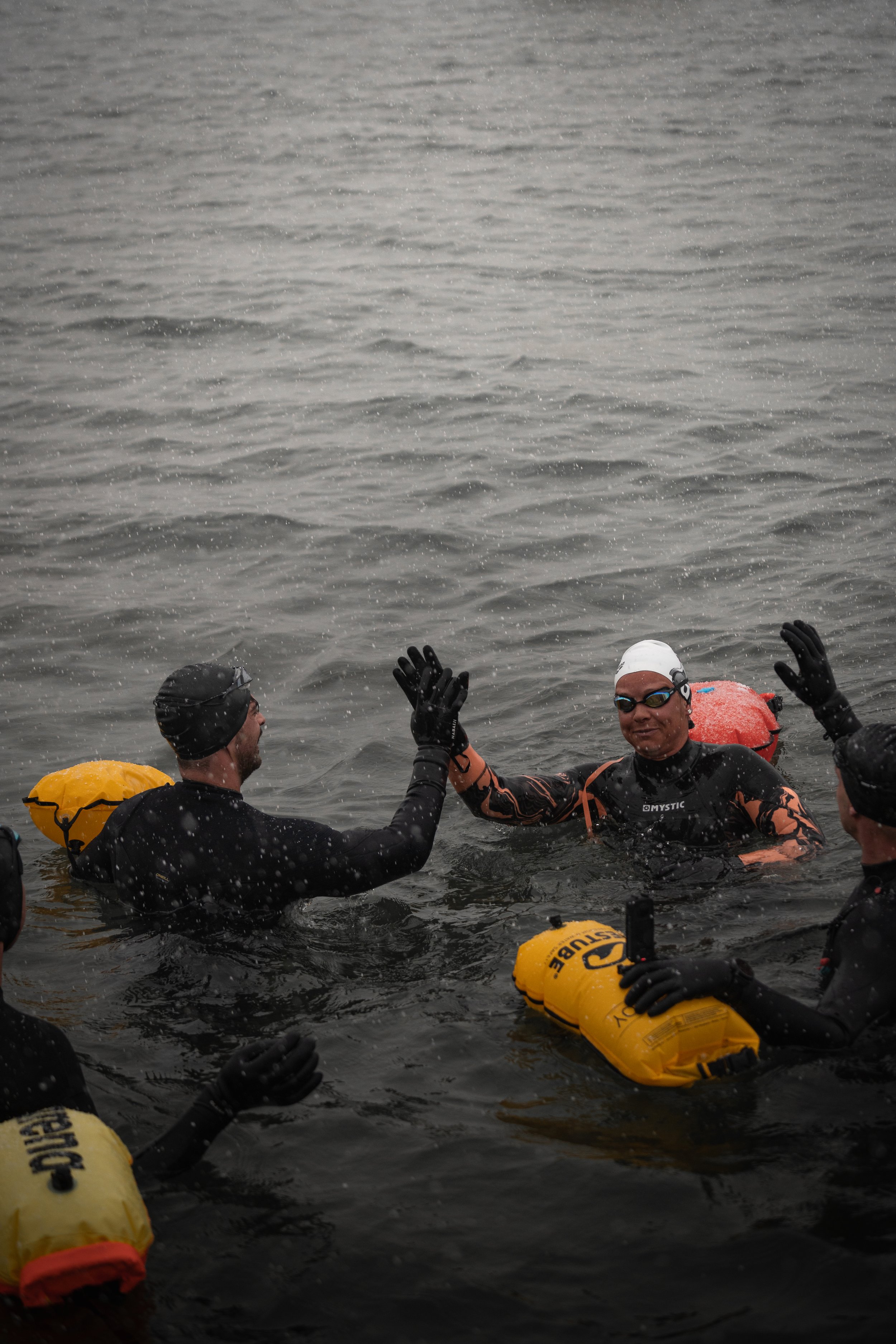 Gruppe von Schwimmern in Neoprenanzügen im Wasser mit Schwimmbojen, geben sich High-Five.