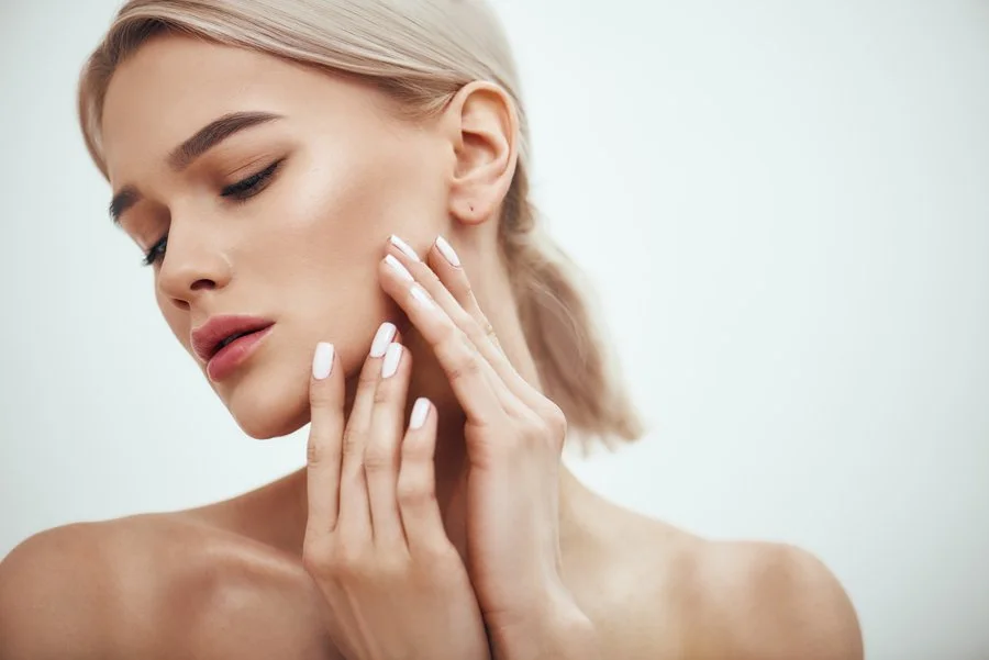 A woman with blonde hair gently touching her neck and cheek, showcasing smooth skin.