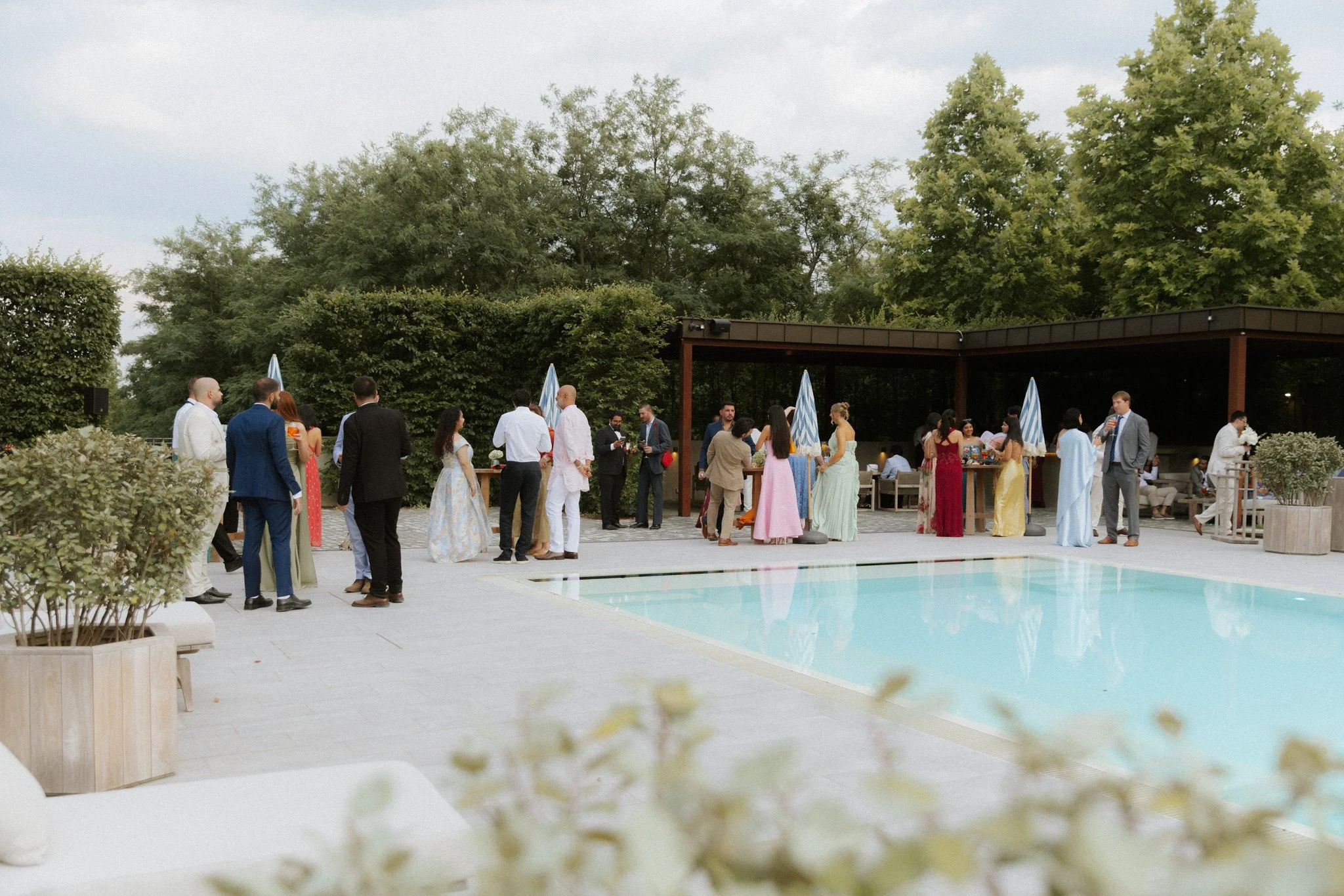 Esküvői cocktail hour a Daalarna Garden medencéje mellett, vendégek koccintanak a kertben