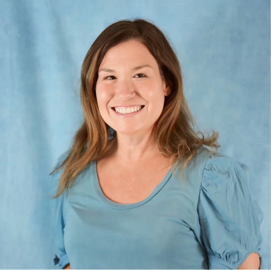 Woman smiling in a blue shirt against a light blue background.