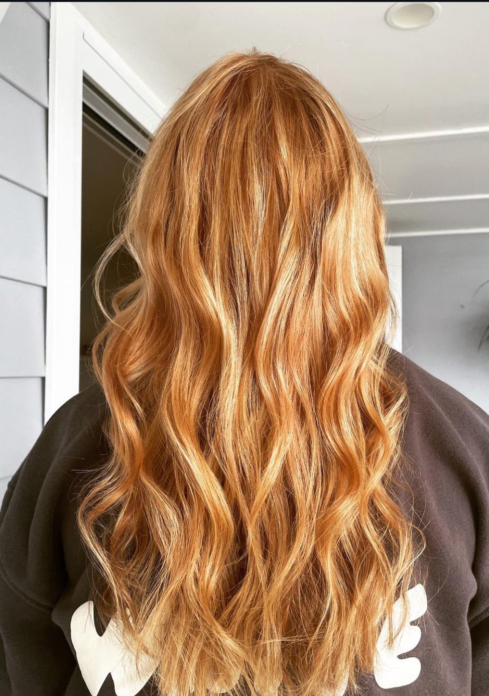 Back view of a person with long, wavy red hair indoors.