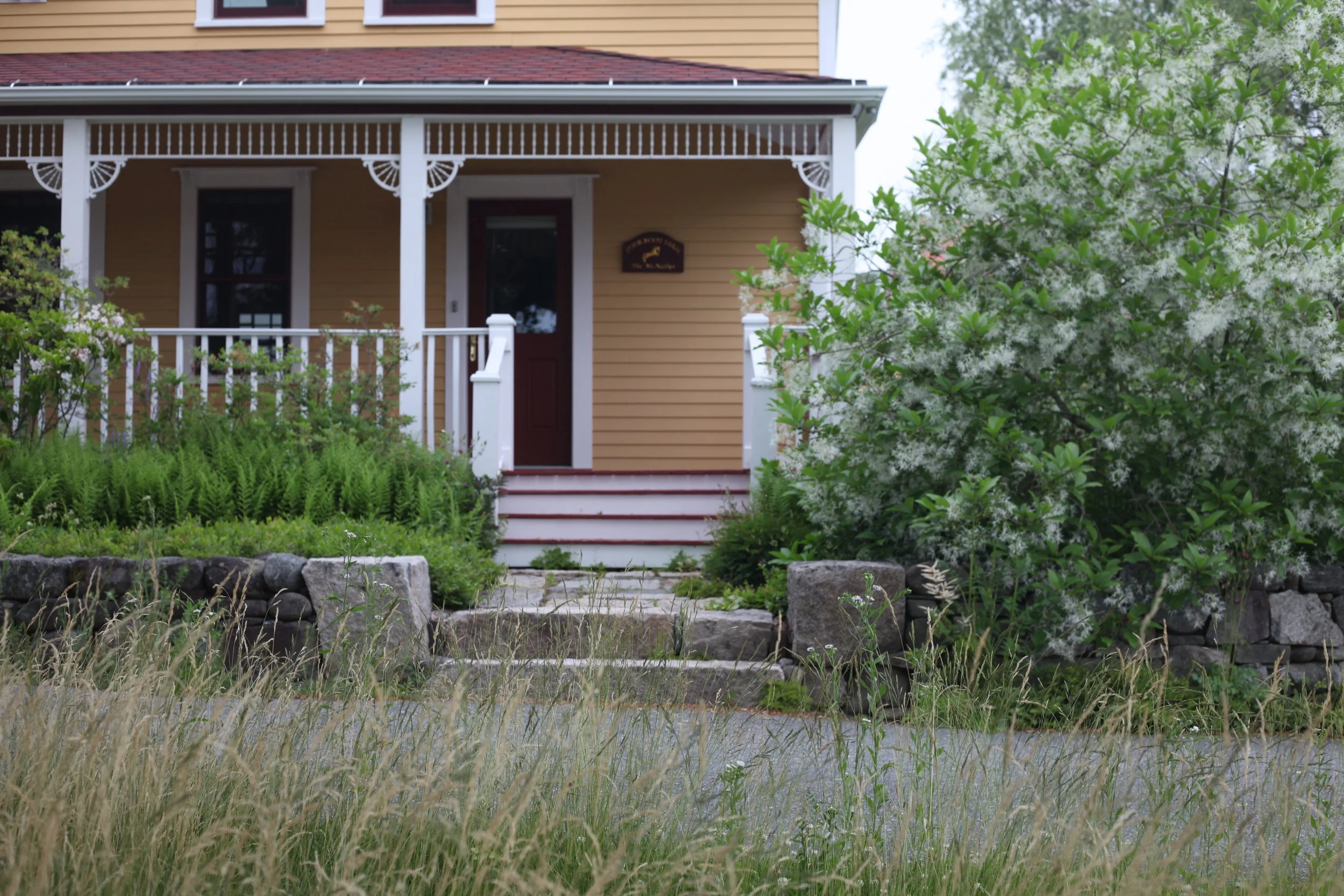 Granite and fieldstone walls frame the entrance walk and native plantings.