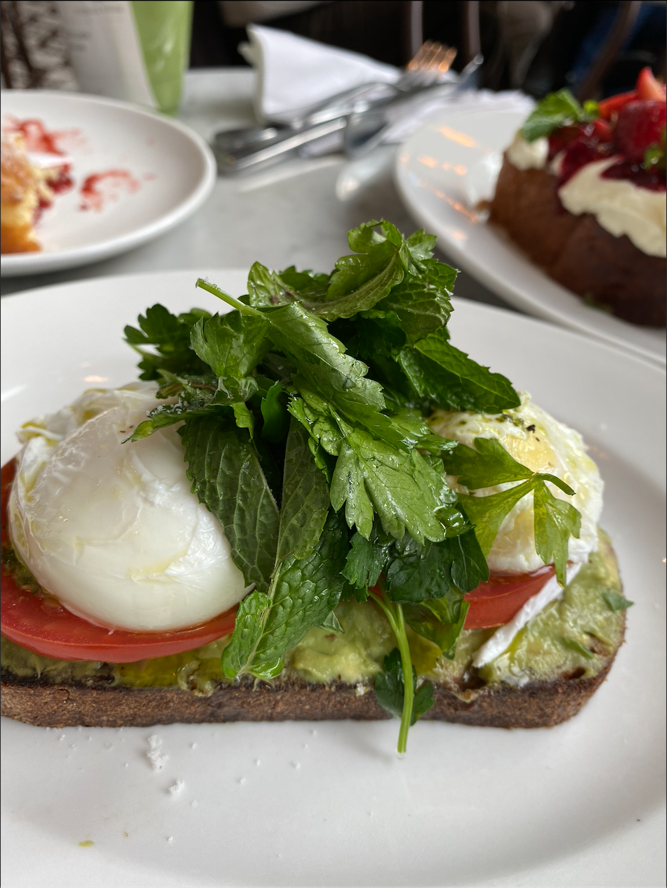 A healthy breakfast dish featuring poached eggs over avocado toast, loaded with fresh green herbs..png