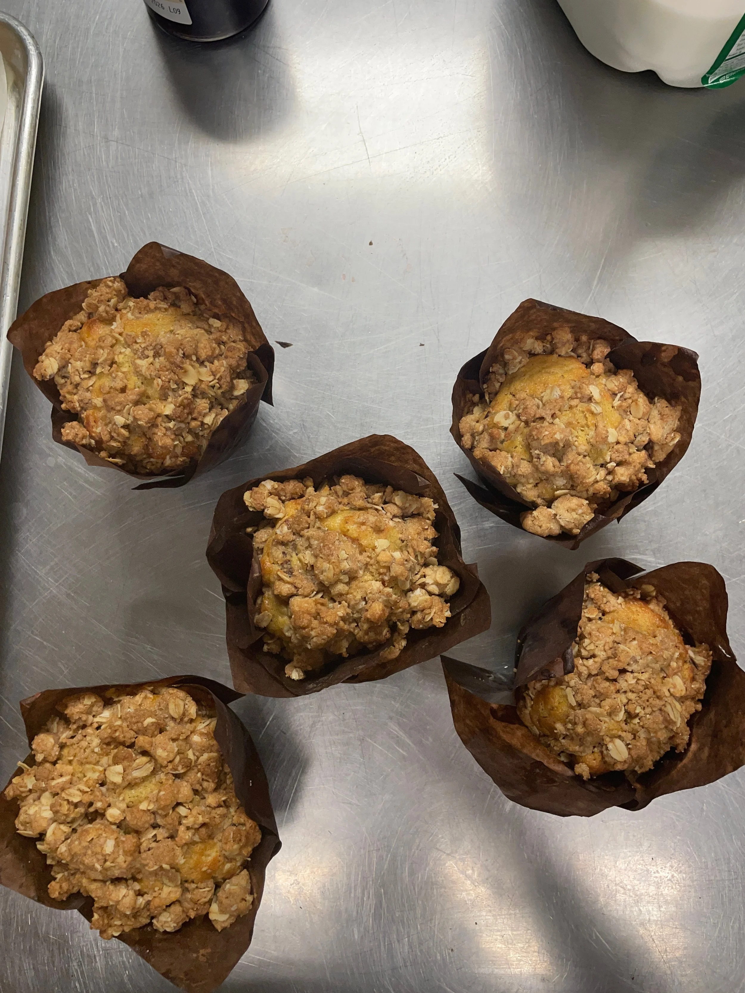 A batch of freshly baked crumb-topped muffins in brown paper liners straight from the bakery kitchen..JPEG