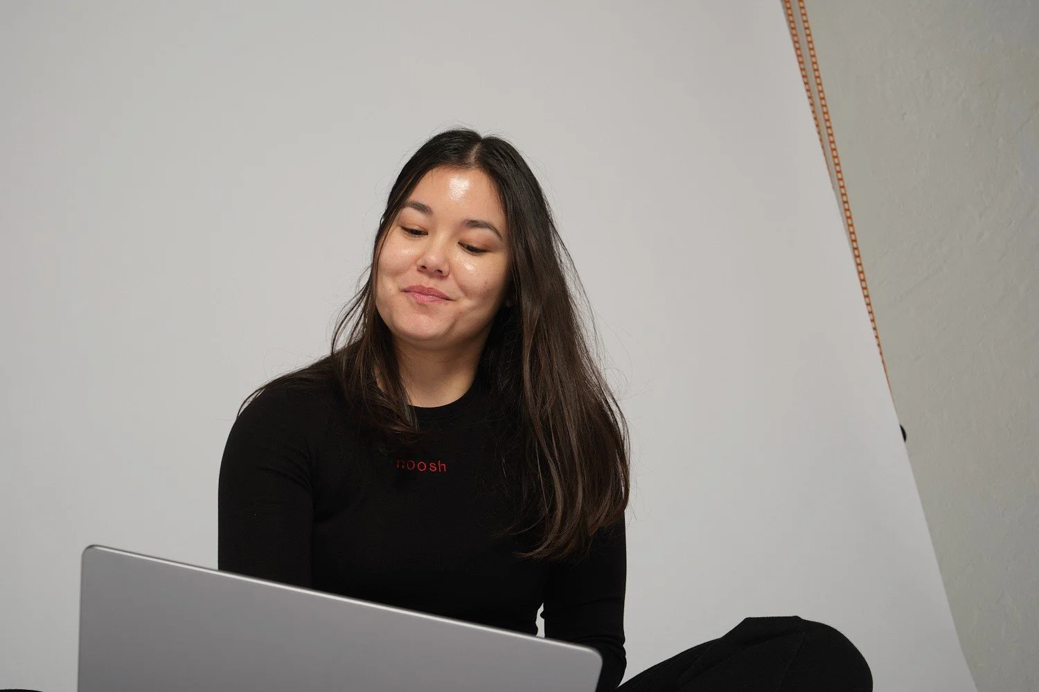 Woman in black shirt looking at laptop, gray background.