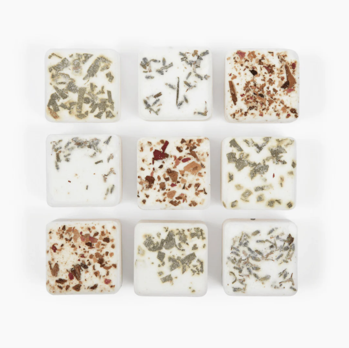 Nine square-shaped bath bombs with various herbs and flower petal inclusions, arranged in a 3x3 grid on a white background.