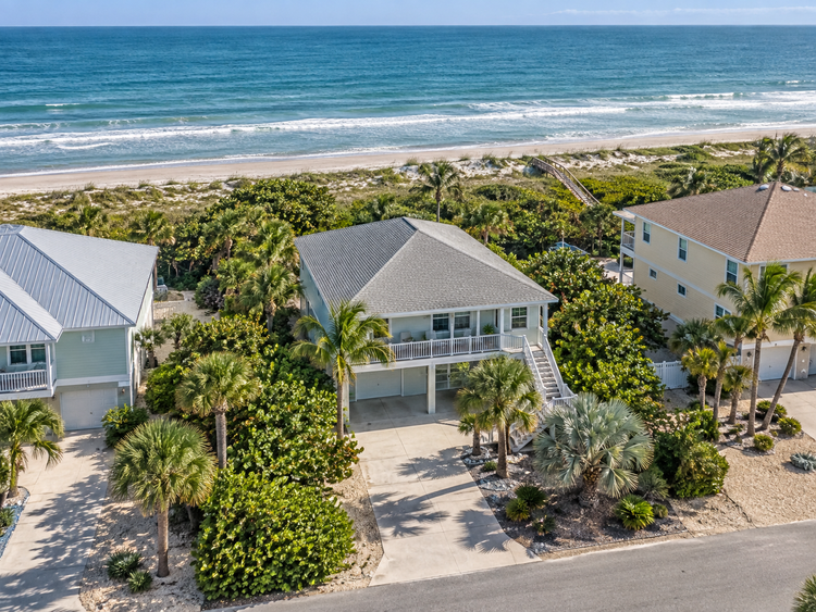 Illustrative drone view of a modest coastal home with blue water behind