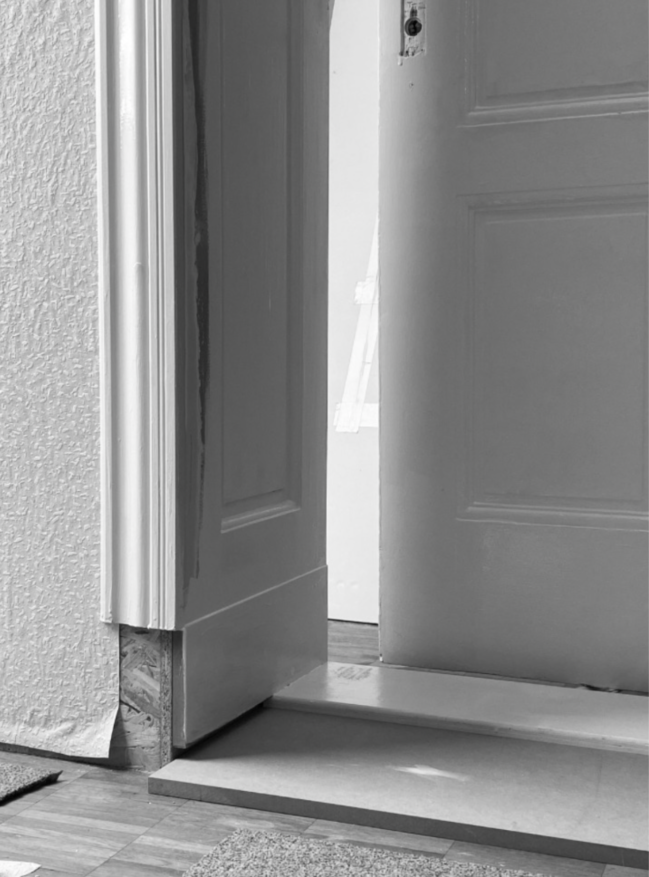 Ein halb offener Holztürrahmen mit einer unvollständigen Tür, die an der Wand befestigt ist, und ein Raum im Hintergrund, vermutlich ein Flur oder ein Zimmer.