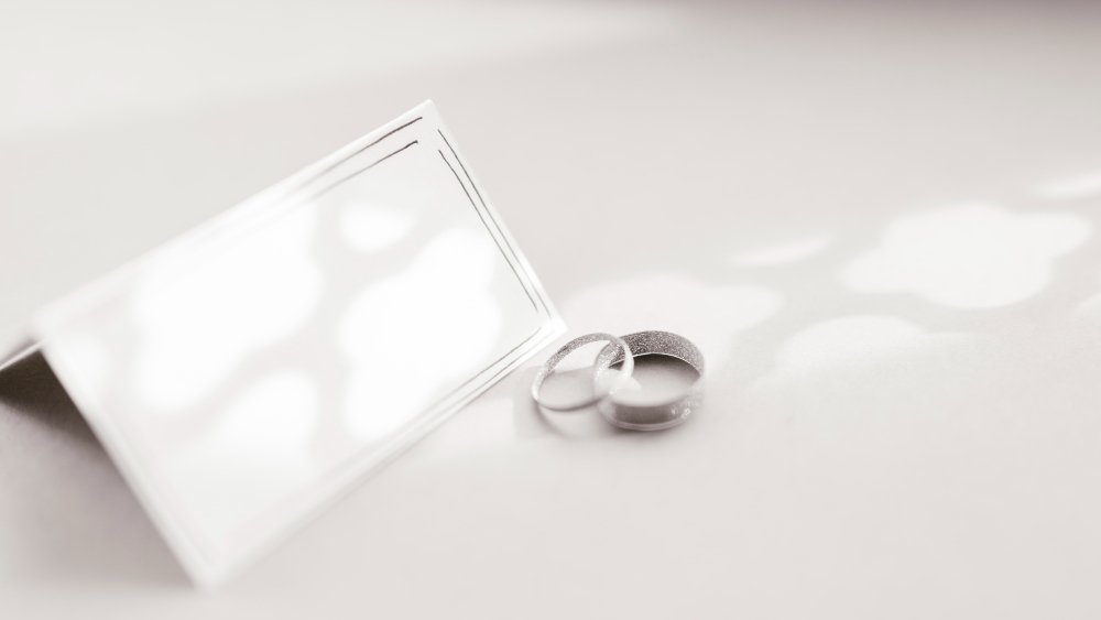 Two silver wedding bands next to an open small silver jewelry box on a white surface.