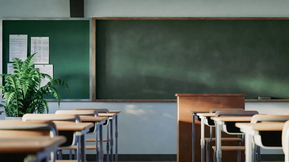 Empty classroom with desks, chairs, a classroom monitor, palms, and a green chalkboard.
