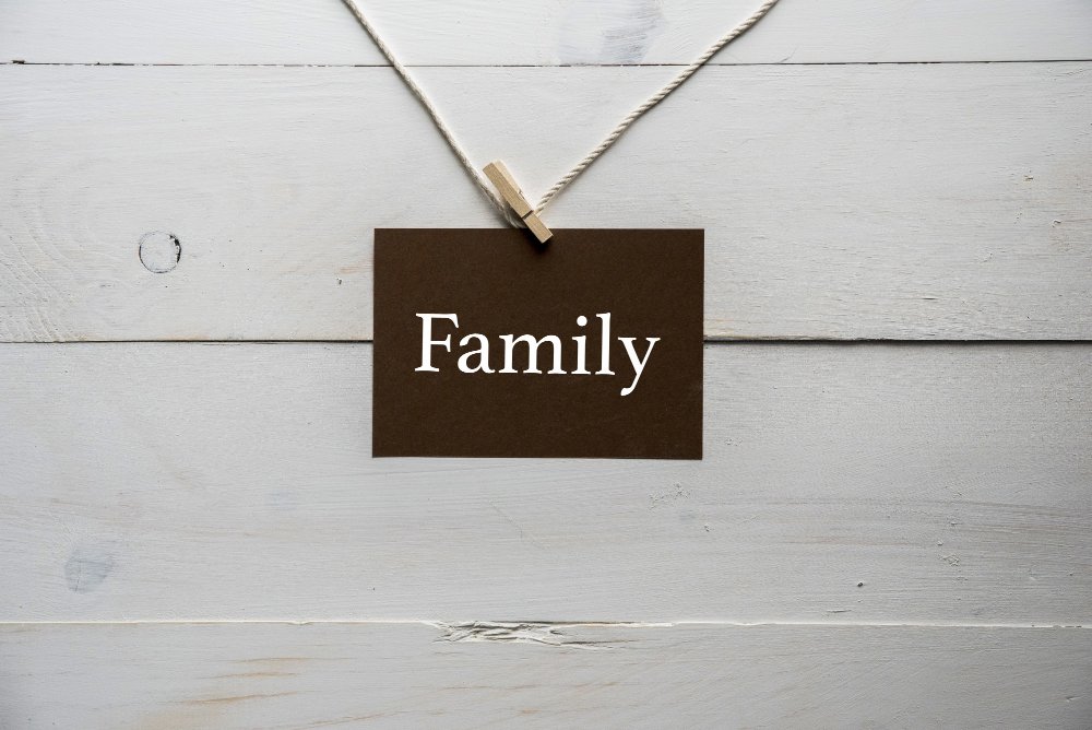 A brown card with the word 'Family' written in white, hanging from a white string and clothespin against a white wooden background.