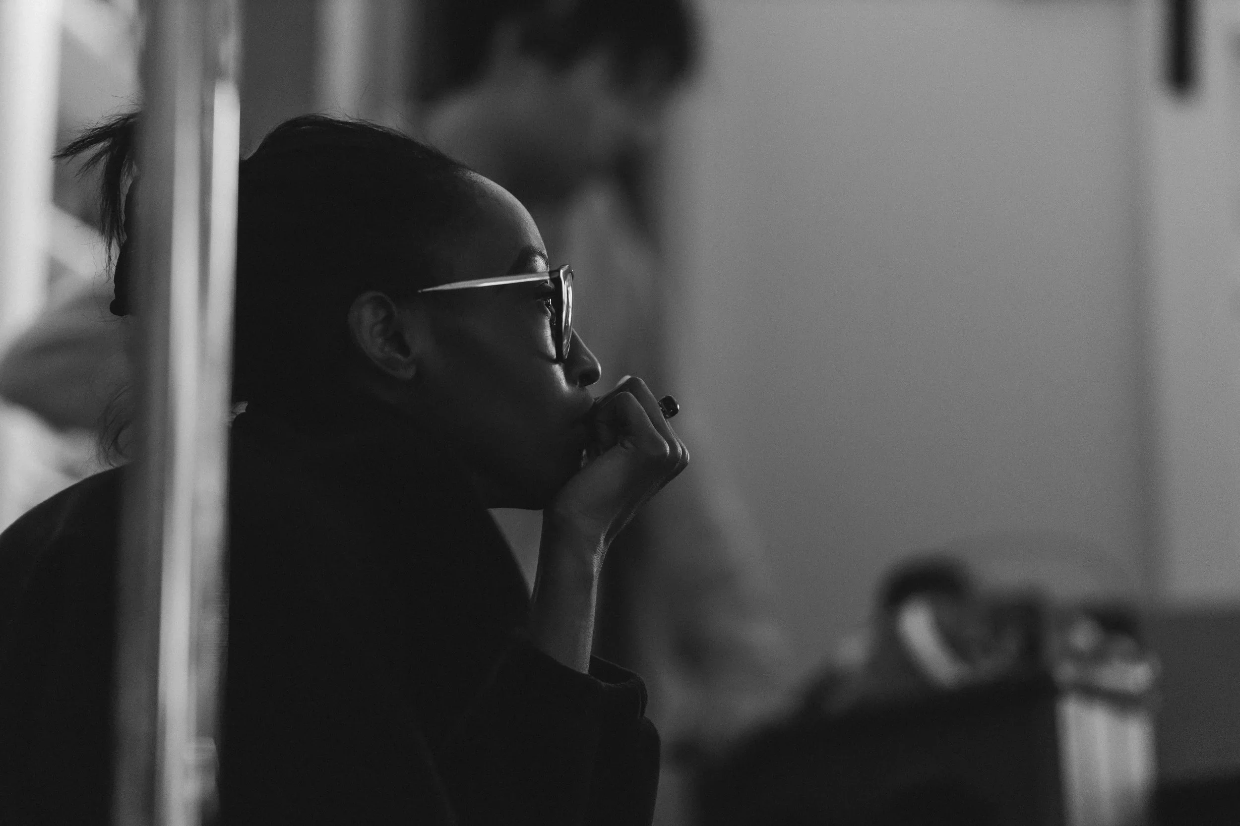A woman with glasses and a ponytail, in profile, deep in thought or conversation, in a grayscale setting.