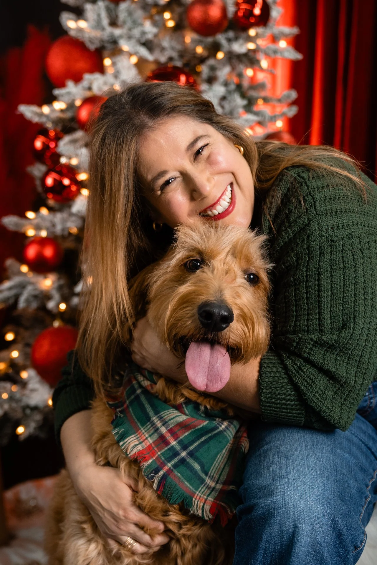 A woman smiling and hugging a dog in front of a decorated Christmas tree