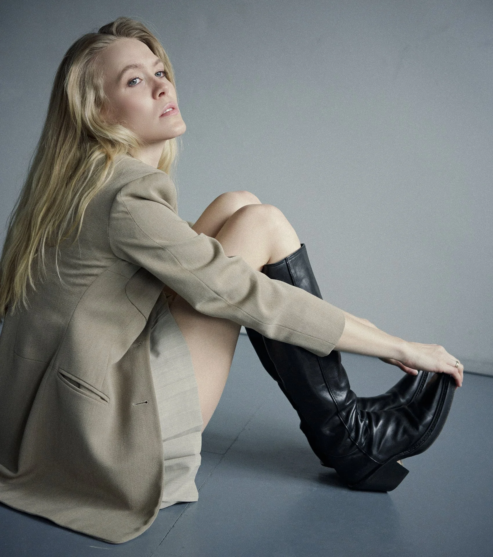 Photographer with photo studio in Munich for personal photo session capturing blond girl sitting on the floor holding her Cossacks shoes wearing jacket