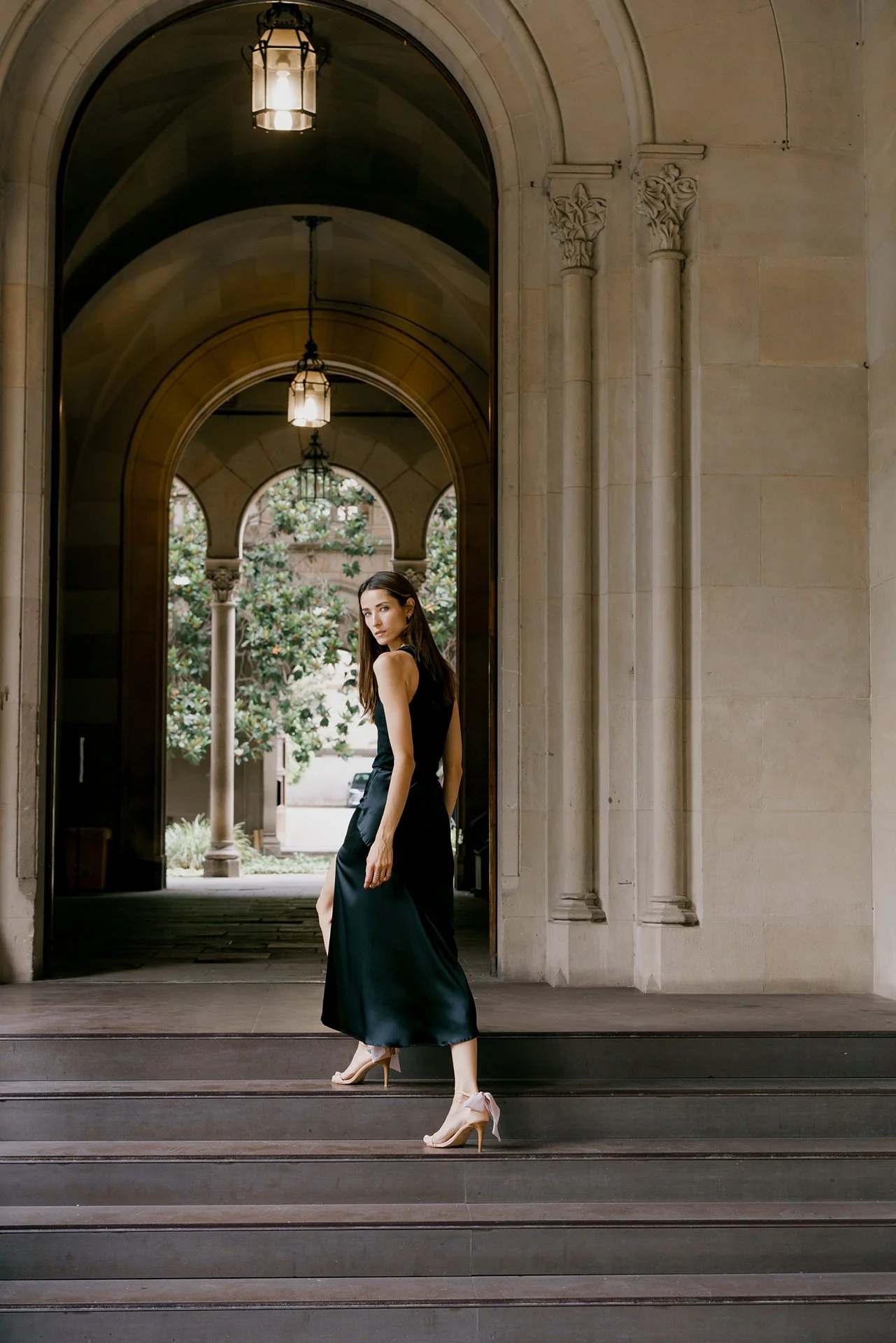 Portrait of a model in beautiful architecture of Milan city in a black dress going up for the stairs and posing for photographer