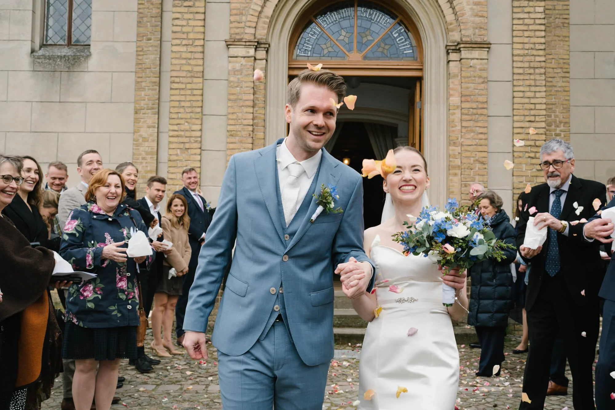bride and groom exiting Dorfkirche Caputh with roses petals