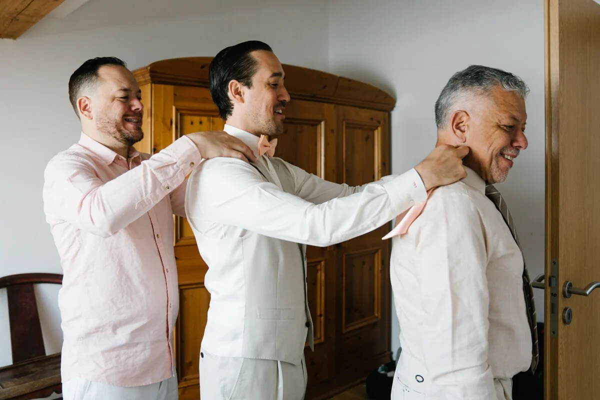 Fun picture of a family members of groom doing their bow tie for the wedding day in Munich one by one in a line