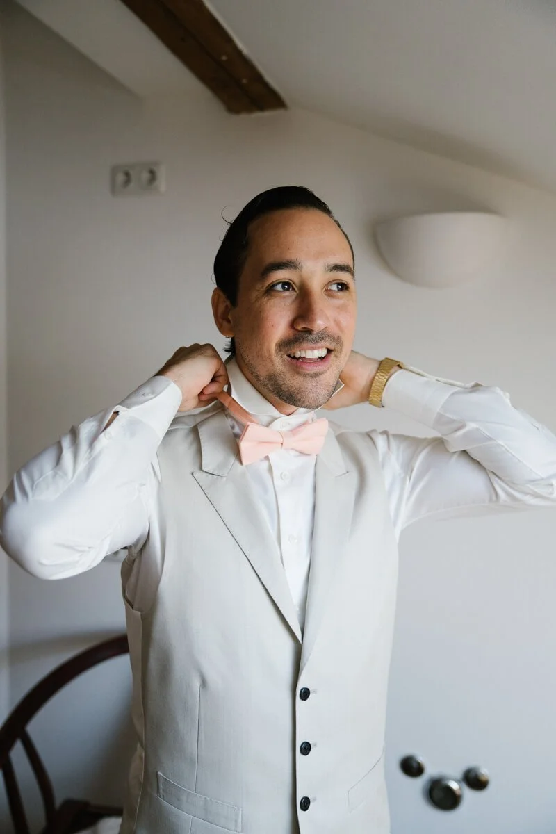Groom puts bow tie to himself during wedding morning in Munich
