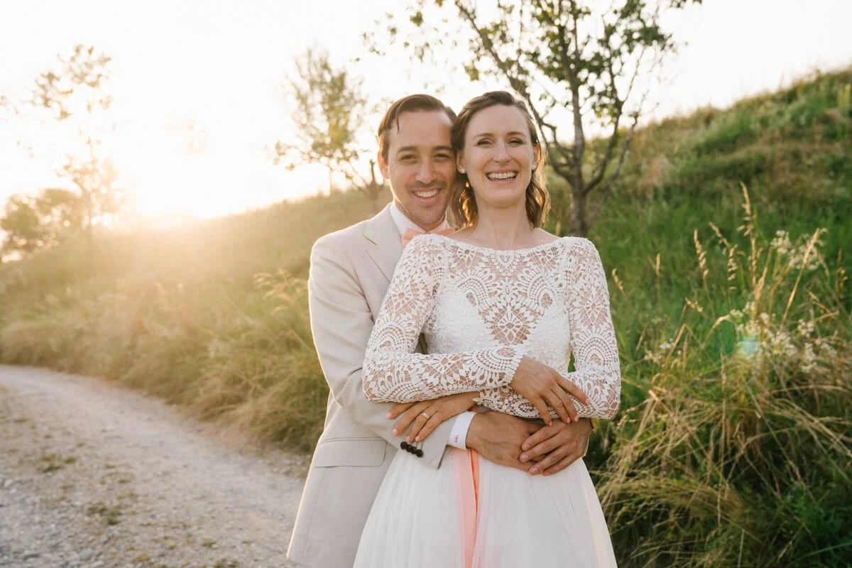 groom is hugging his bride from the back during sunset