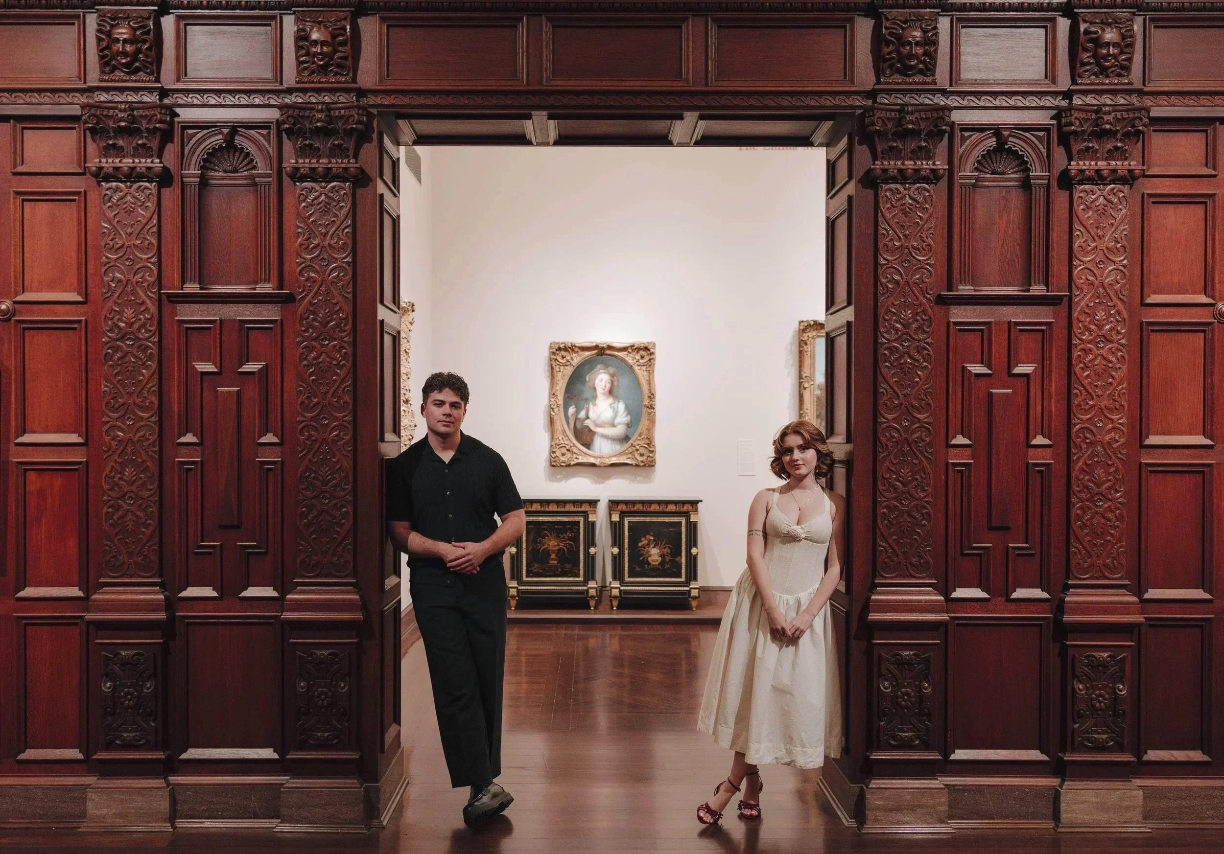 A man and a woman standing in a grand art gallery with wood doors and framed paintings. DOCUMENTARY STYLE, EDITORIAL STYLE