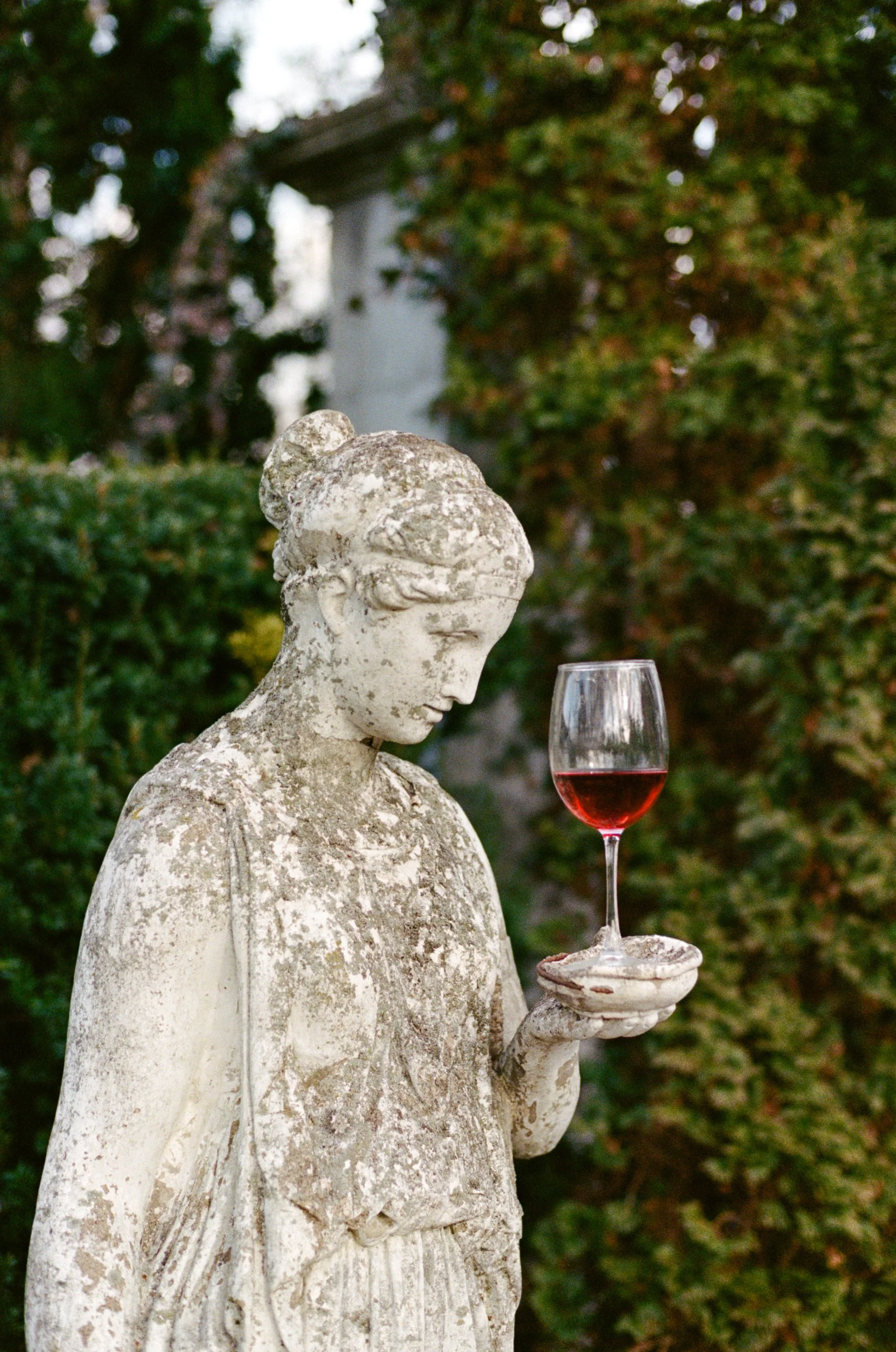An ancient stone statue of a woman holding a wine glass filled with red wine.