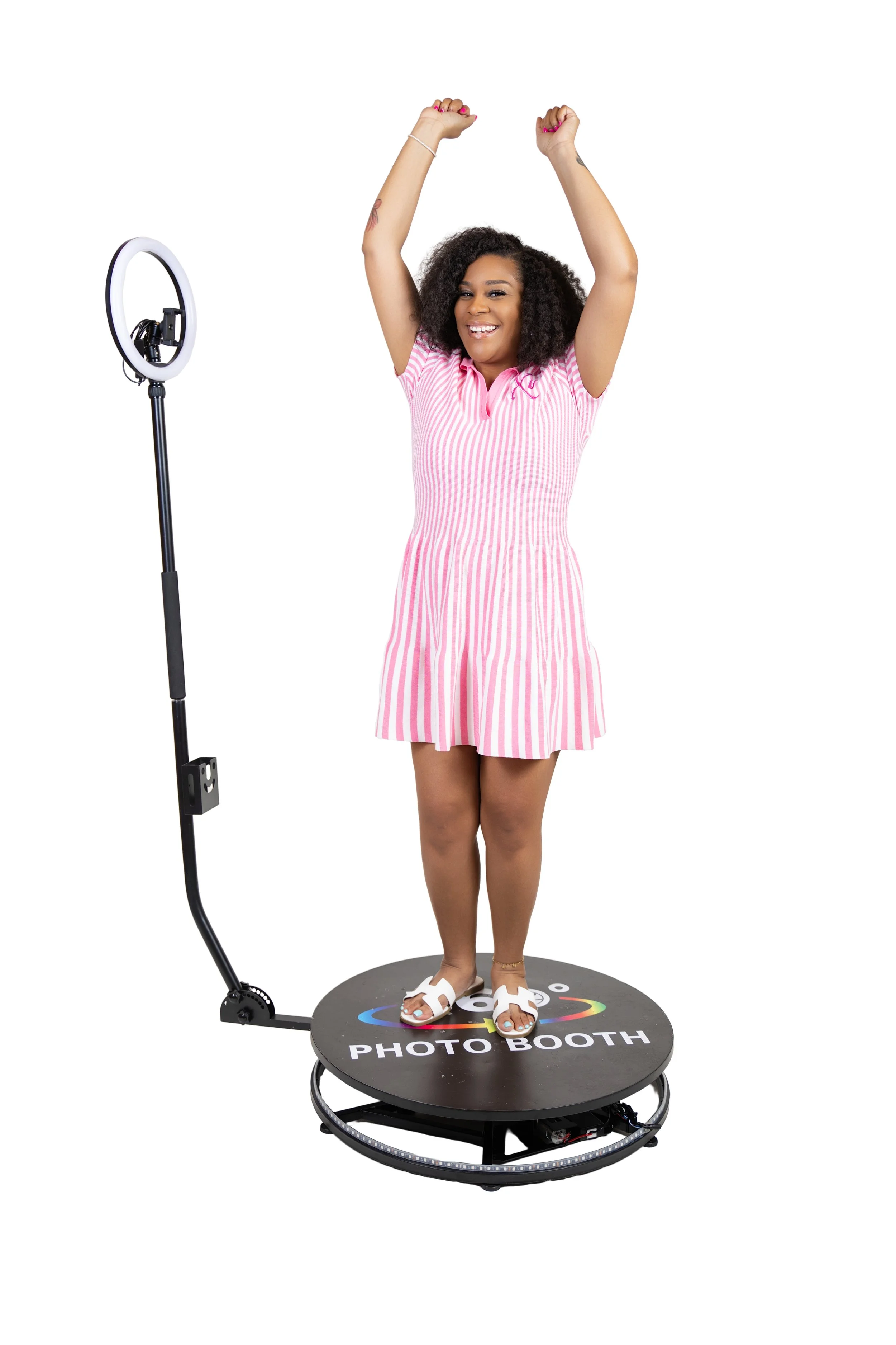 Woman on a digital photo booth platform smiling and raising her arms, wearing a pink and white striped dress.