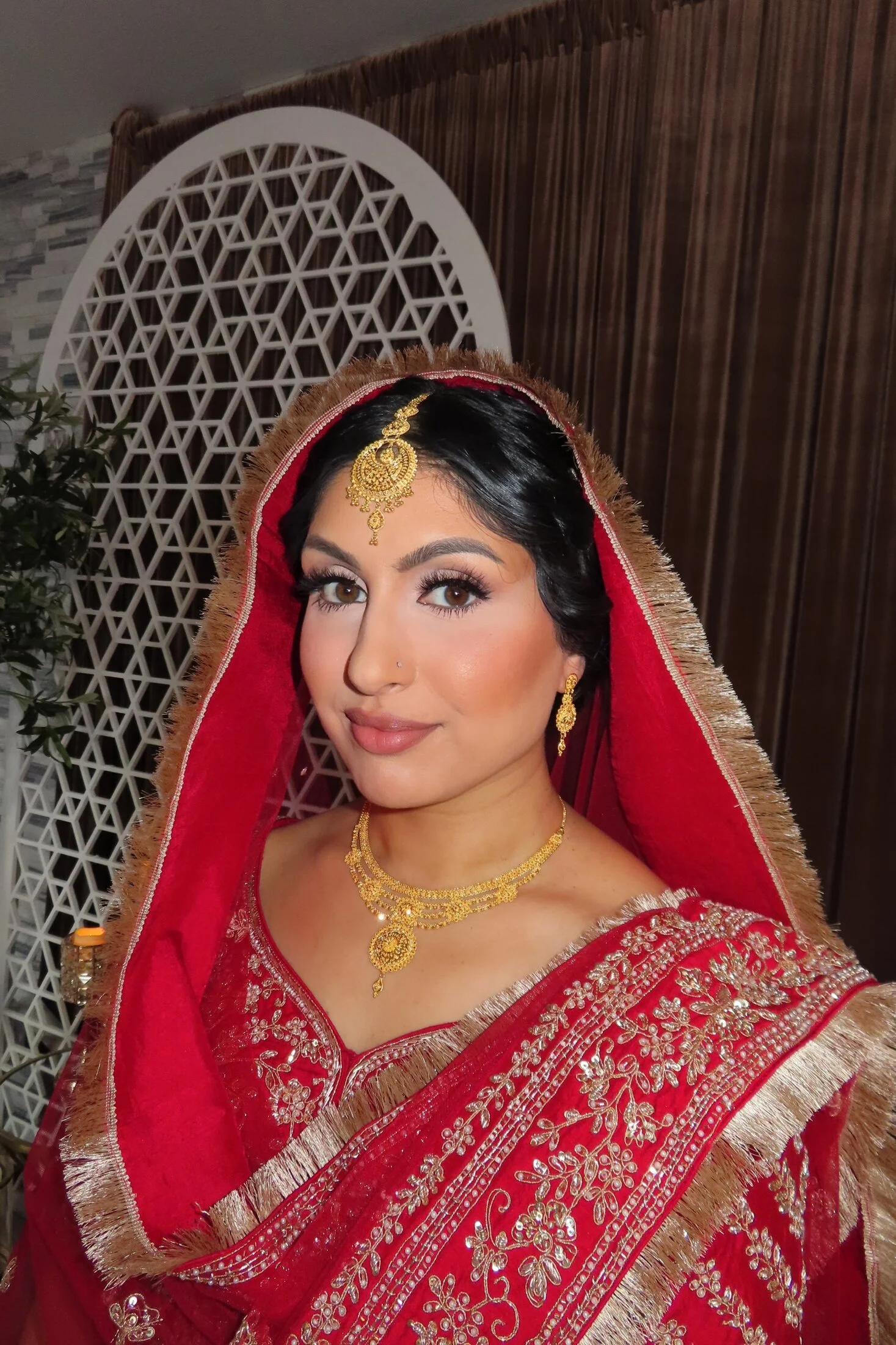 Classic South Asian bridal makeup by Glam by Manpreet with a red dupatta and gold jewelry.