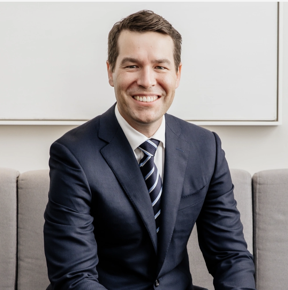 Dr Matthew Peters in a navy suit and striped tie sitting on a sofa