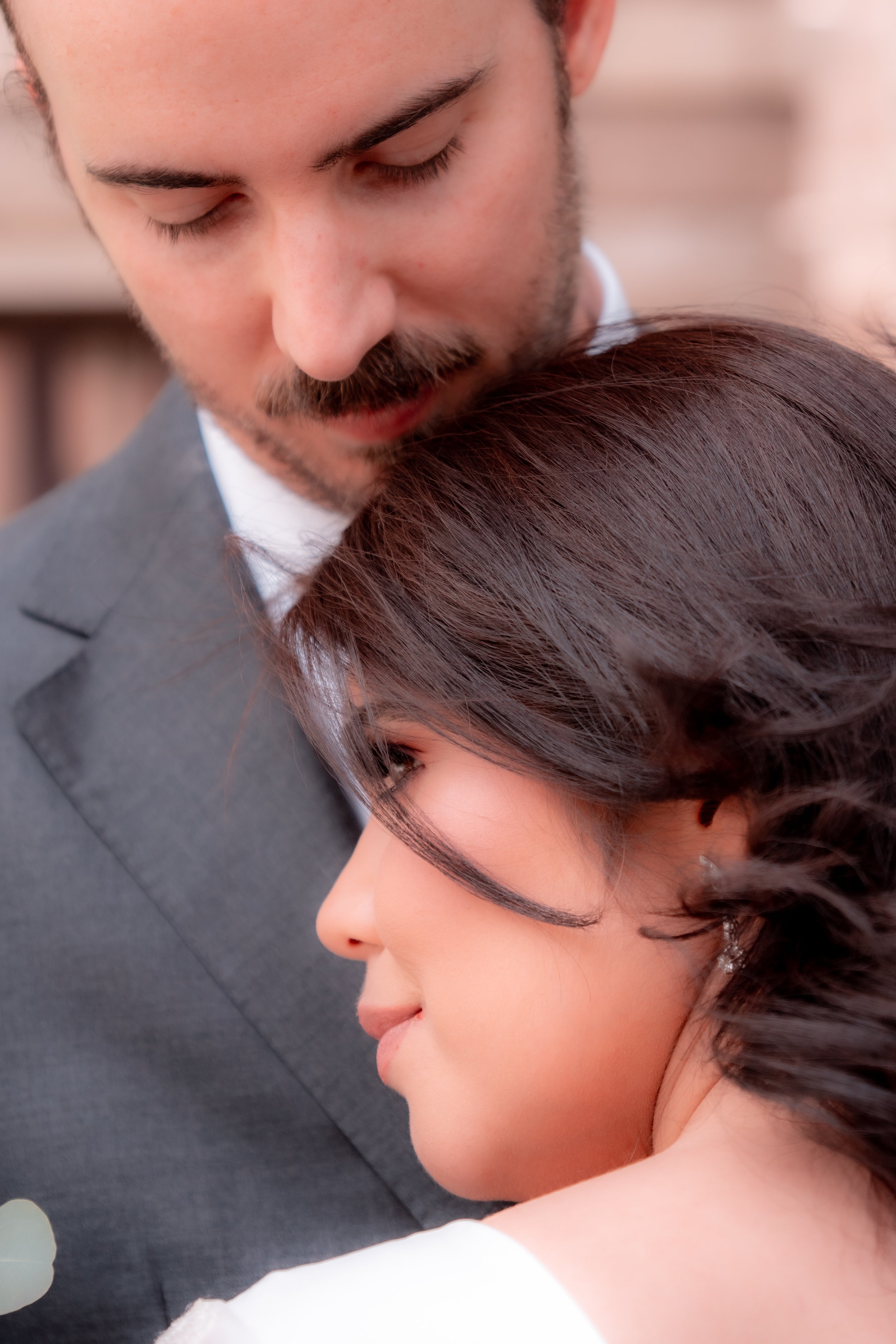 A man and woman share an intimate moment, with the man gently leaning his forehead against the woman's head while she has her eyes closed and smiles softly.