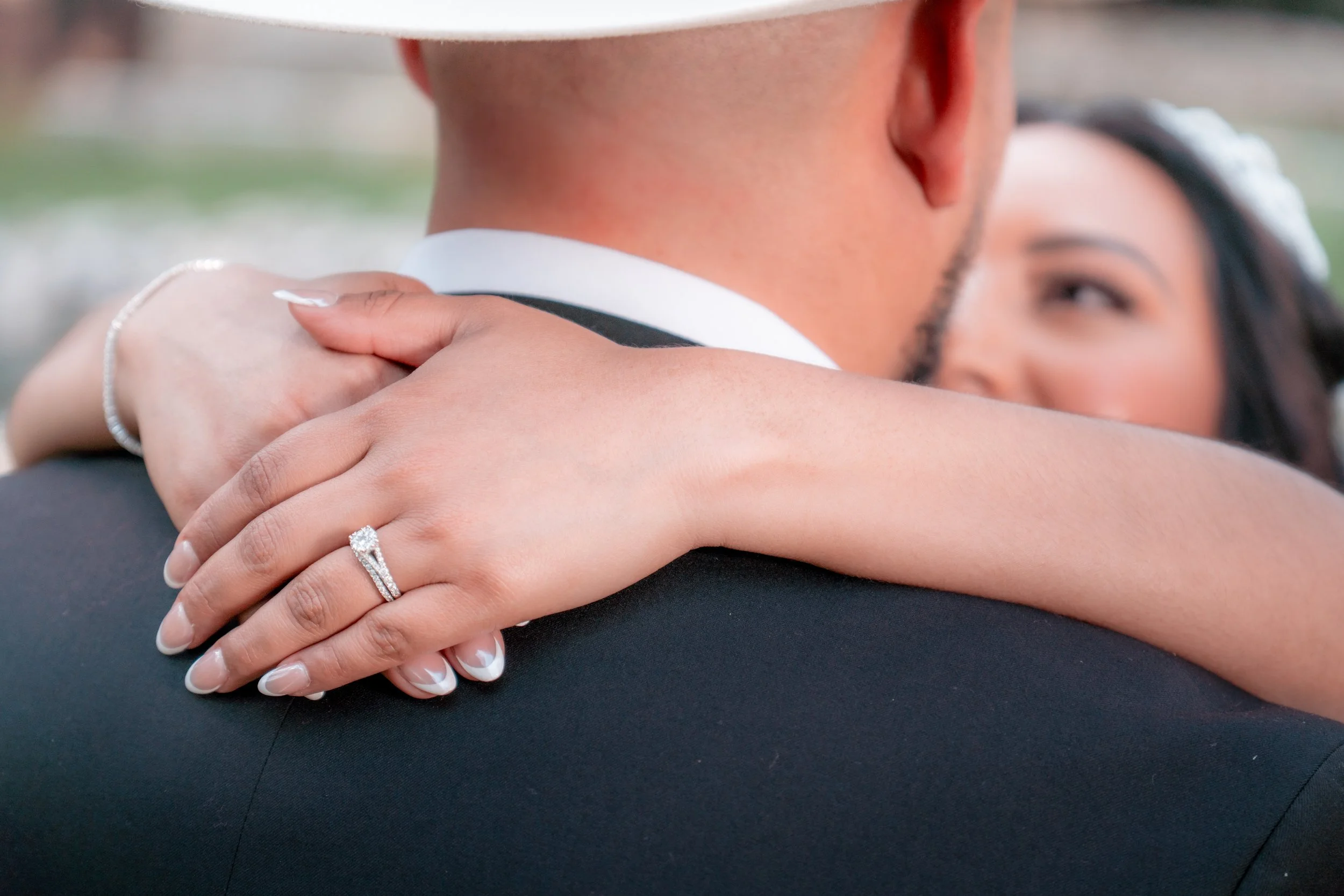 Close-up of a woman with a wedding ring on her finger resting on a man's shoulder during a wedding or engagement photo