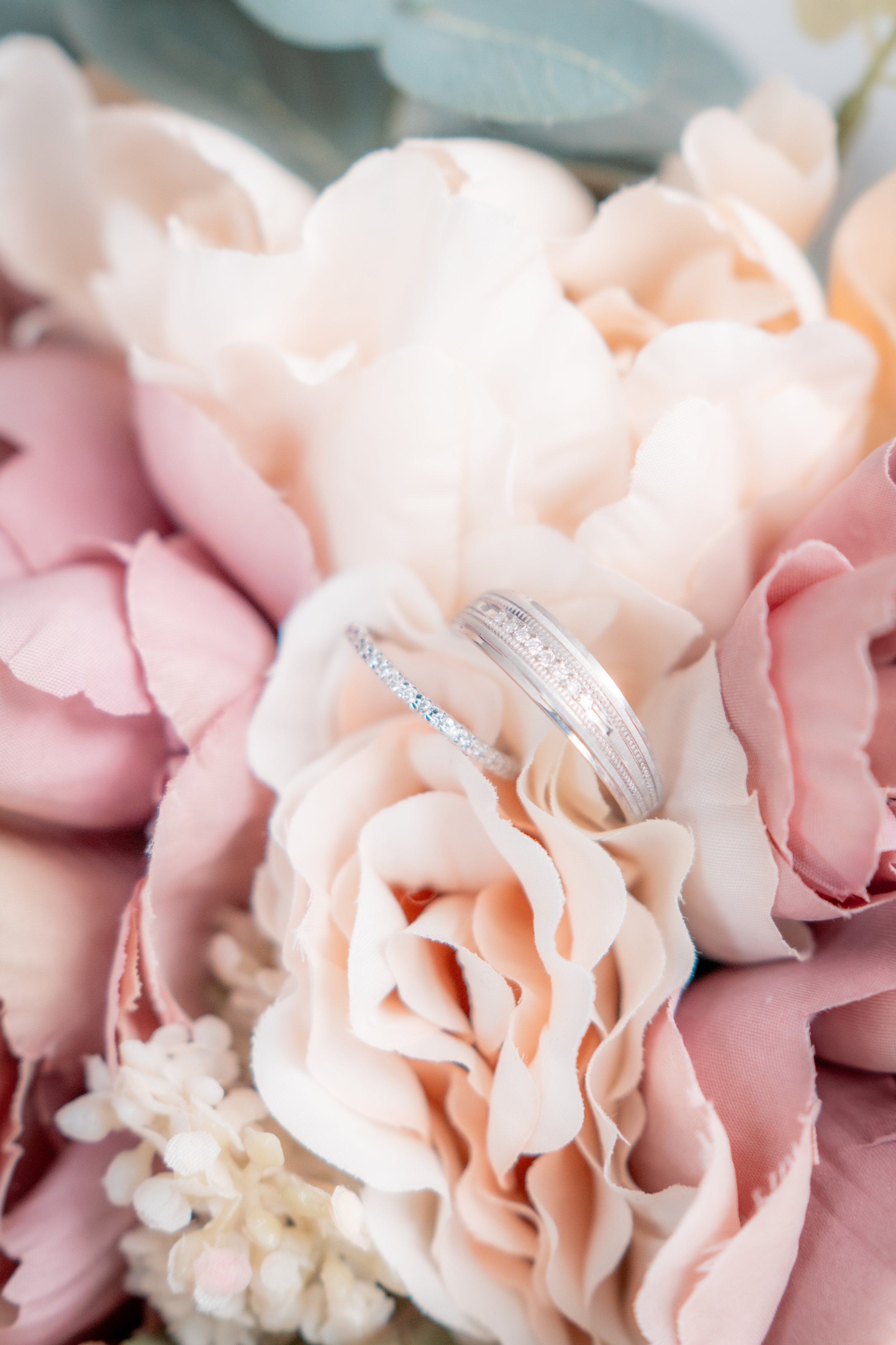 Wedding rings placed on a light pink and white flower surrounded by pink blossoms.